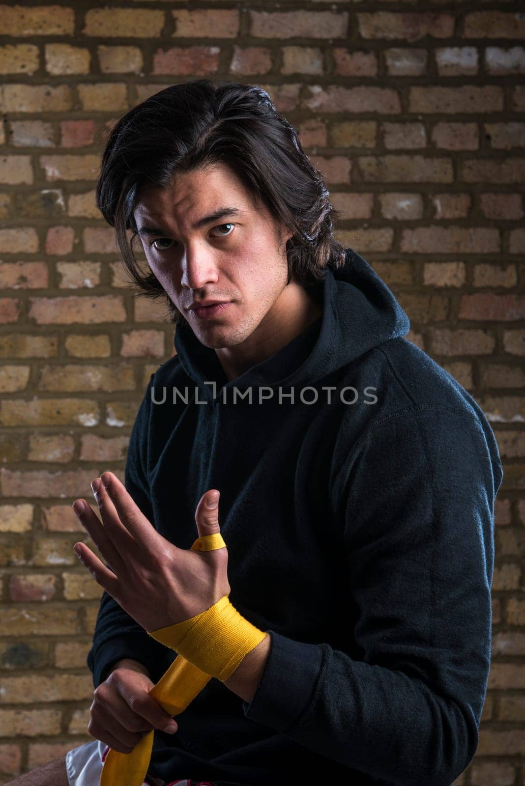 Young Malaysian boxer  wearing hoodie and wrapping straps around hands