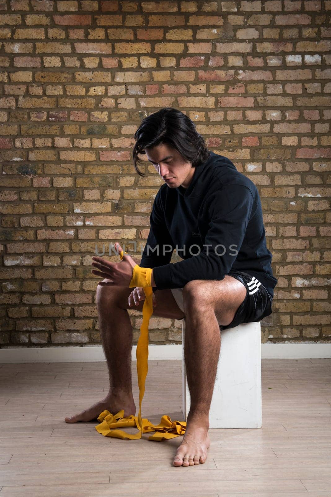 Young Malaysian boxer  wearing hoodie and wrapping straps around hands