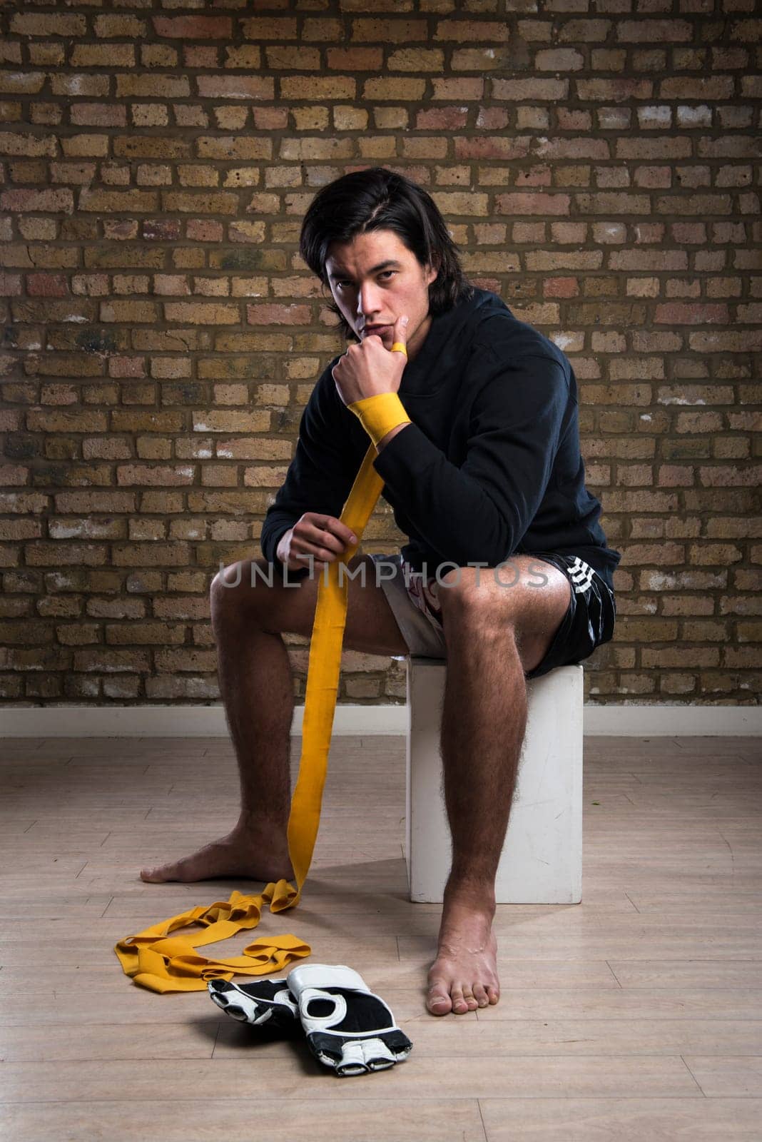 Young Malaysian boxer  wearing hoodie and wrapping straps around hands