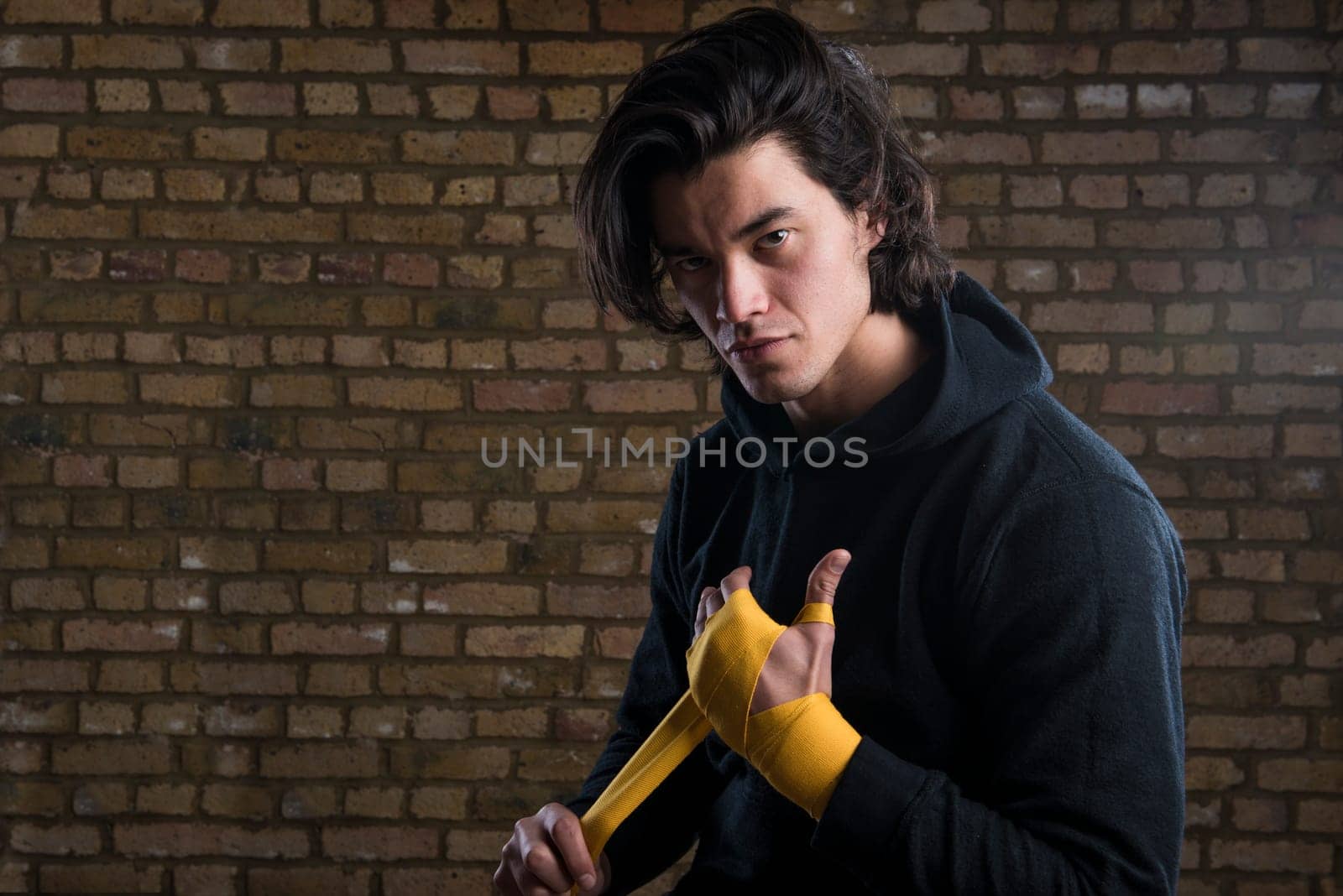 Young Malaysian boxer  wearing hoodie and wrapping straps around hands