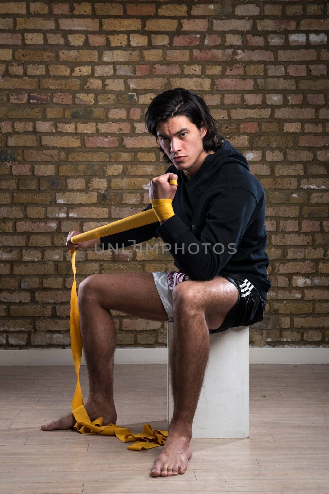 Young Malaysian boxer  wearing hoodie and wrapping straps around hands