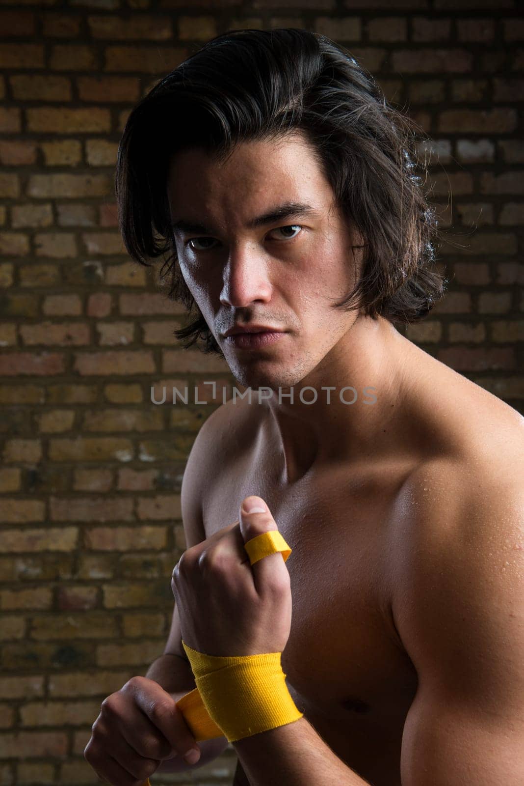 Bare chested young Malaysian boxer wrapping straps around hands