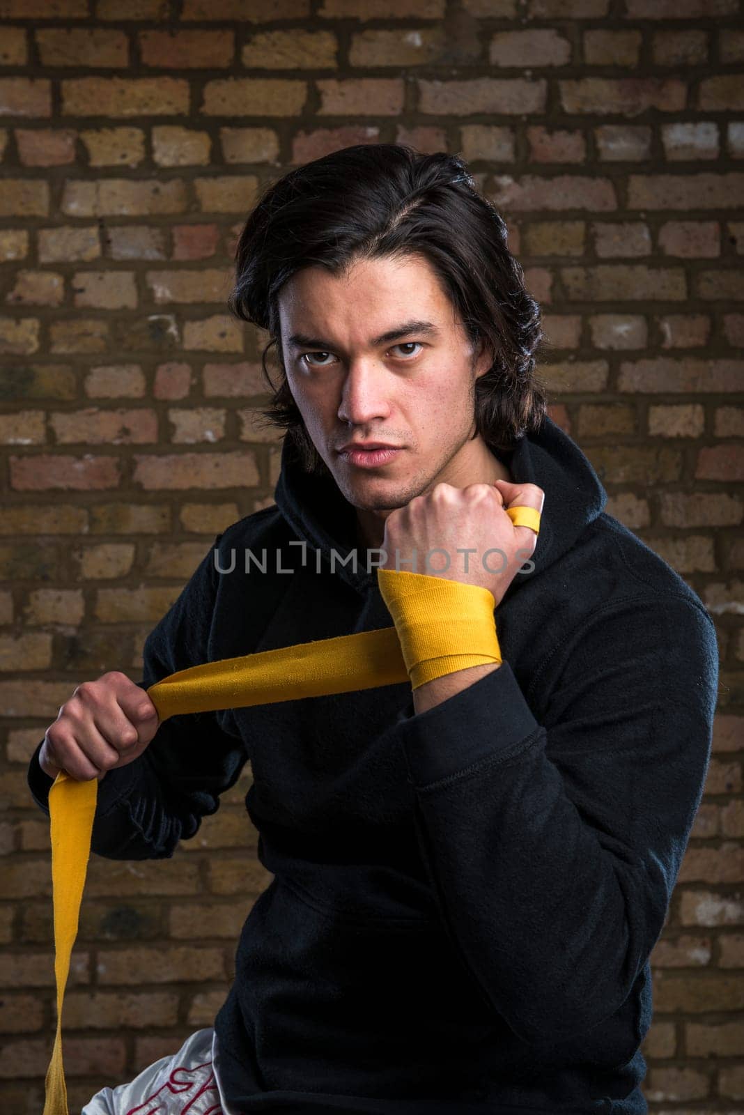 Young Malaysian boxer  wearing hoodie and wrapping straps around hands
