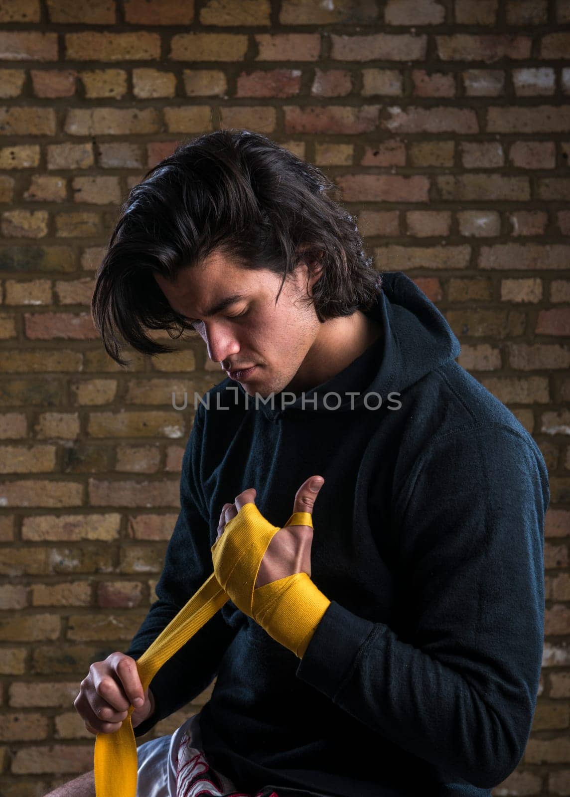 Young Malaysian boxer  wearing hoodie and wrapping straps around hands
