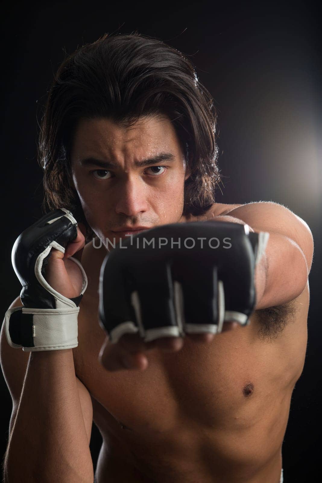 Bare chested young Malaysian boxer punching in the direction of the camera with fingerless gloves