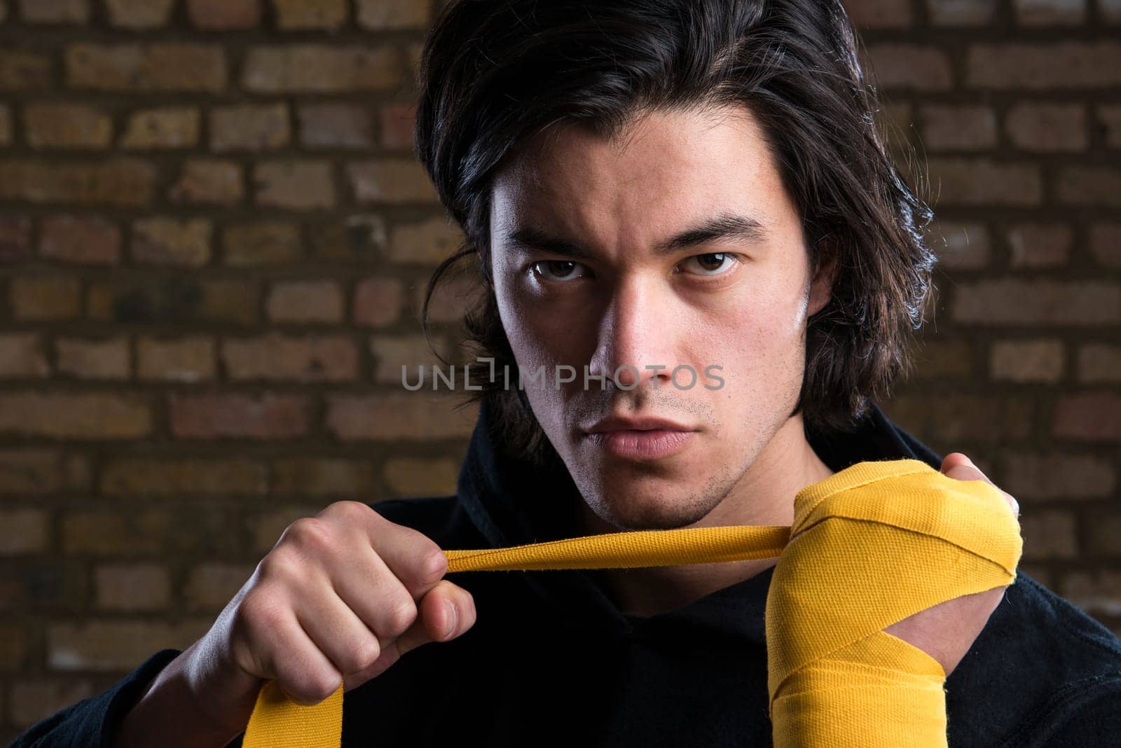 Young Malaysian boxer  wearing hoodie and wrapping straps around hands