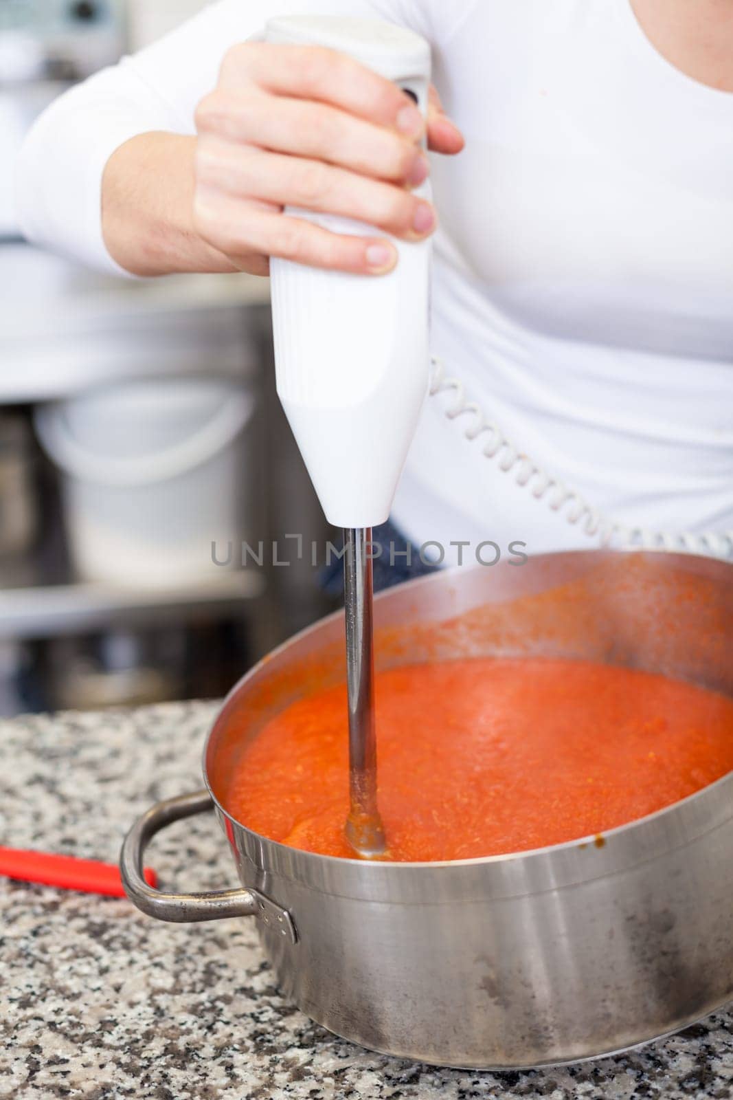 female chef in the restaurant kitchen gastronomy pureed passes tomatoes to a sauce puree tomato sauce