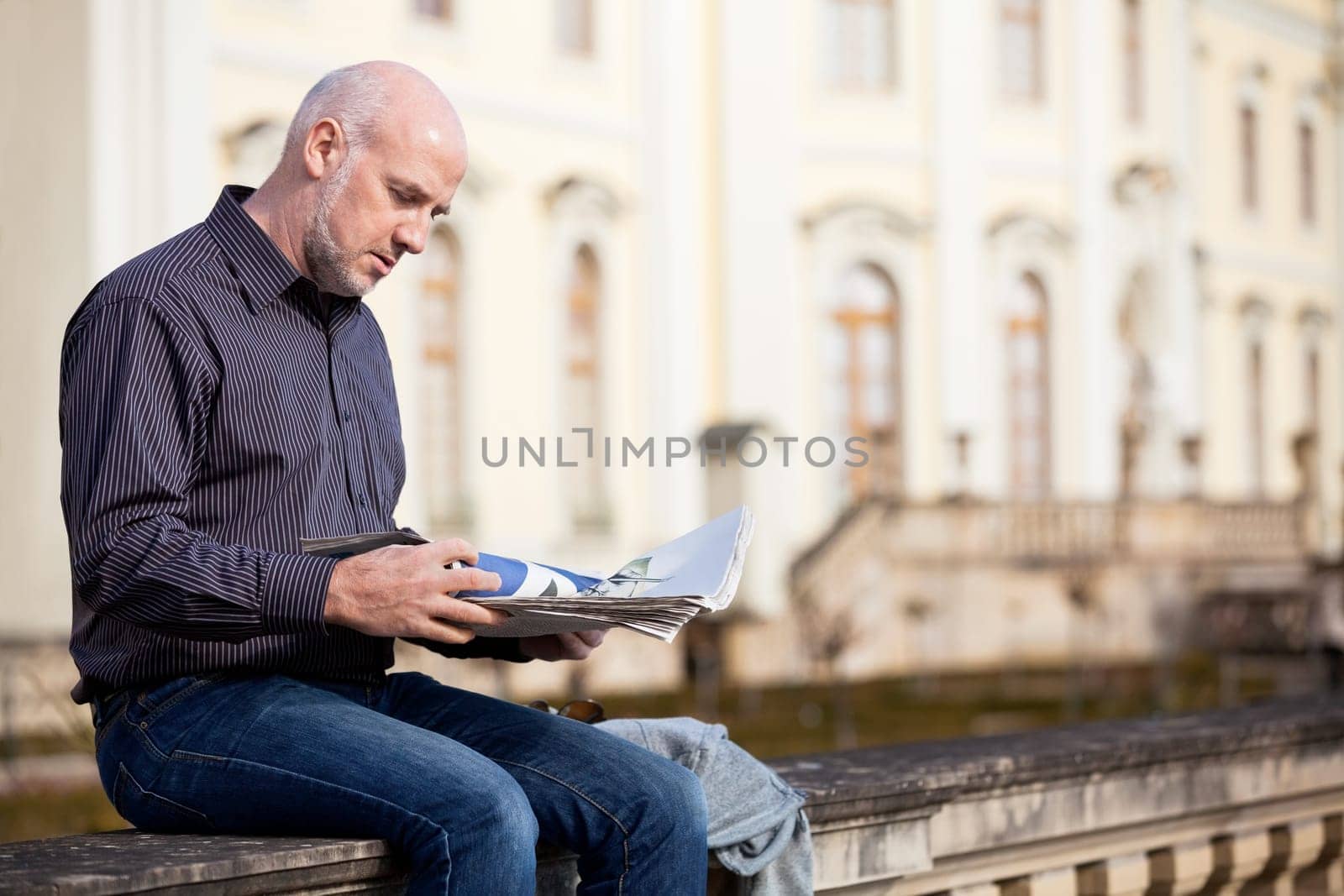 adult older man sitting outdoors reads a newspaper news free time