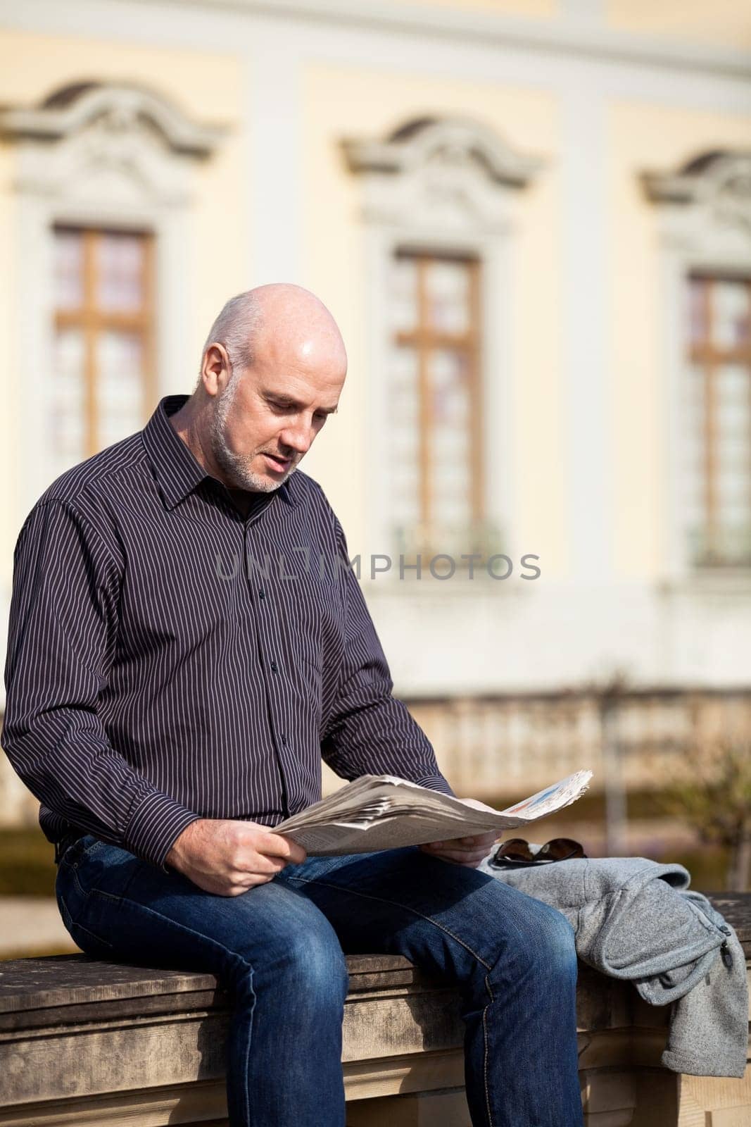 adult older man sitting outdoors reads a newspaper news free time