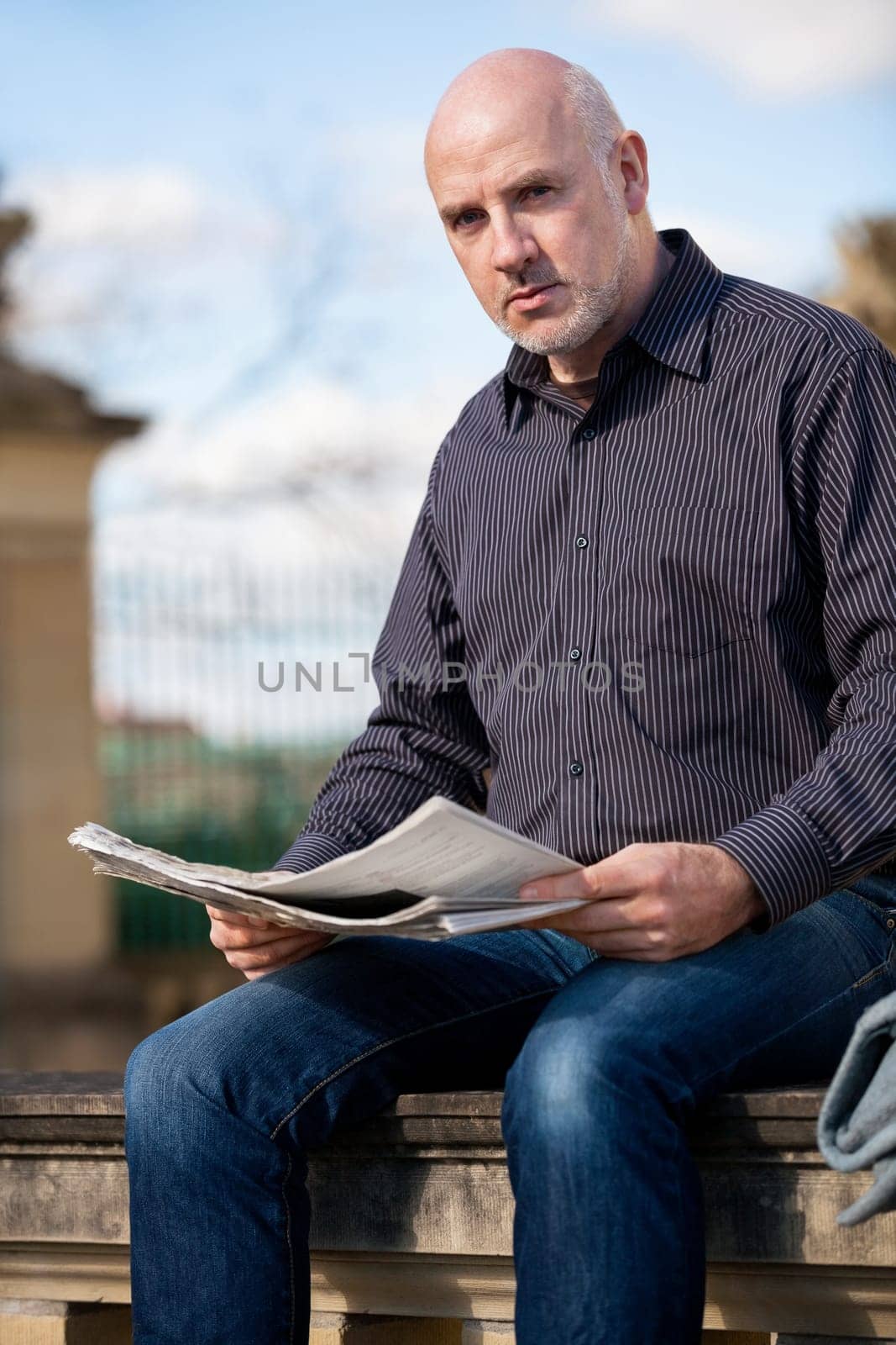 adult older man sitting outdoors reads a newspaper news free time