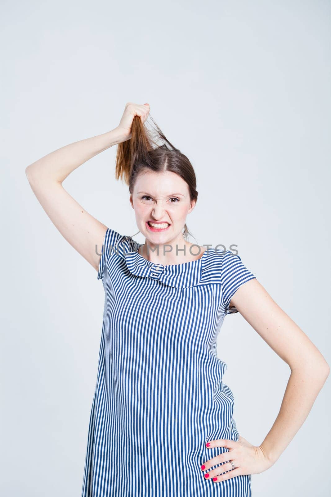 Studio portrait of attractive and stylish woman playfully pulling her hair while grimacing