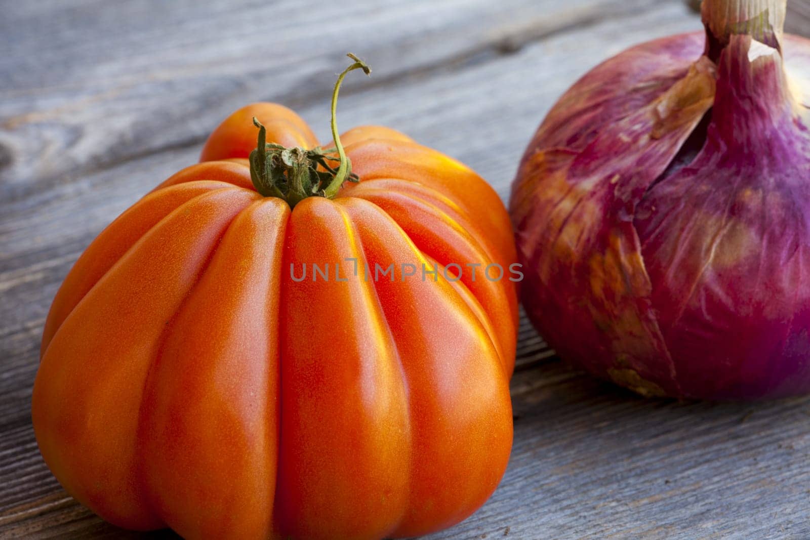 One Beefsteak Tomato and a whole red Onion from Weekly Market in South France on a old wooden Table