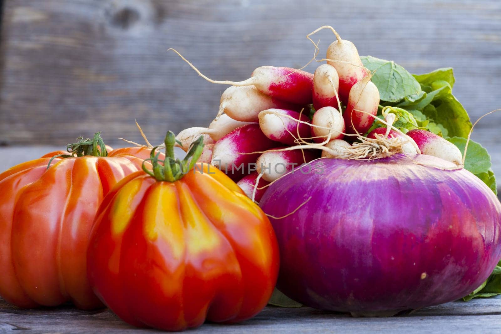 Coeur de Boeuf Tomatoes, large red Onions and Radishes fresh from the Weekly Market on a old wooden Table