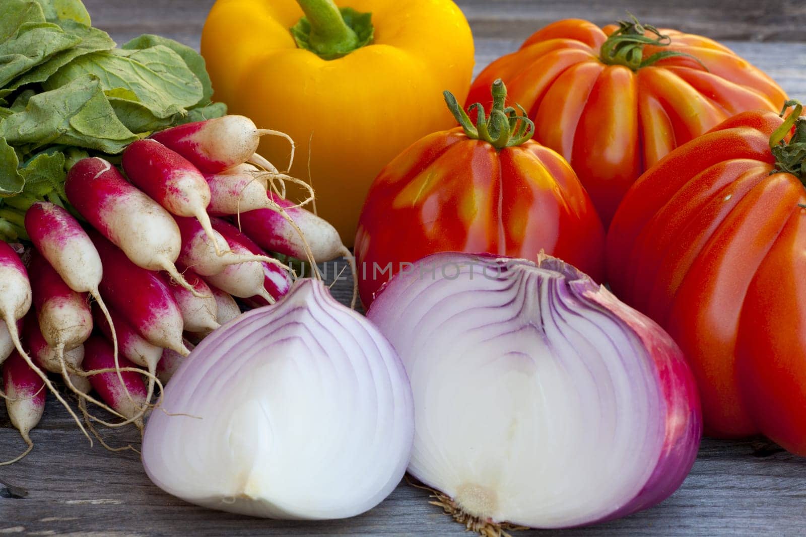Coeur de Boeuf Tomatoes, large red Onions and Radishes fresh from the Weekly Market on a old wooden Table