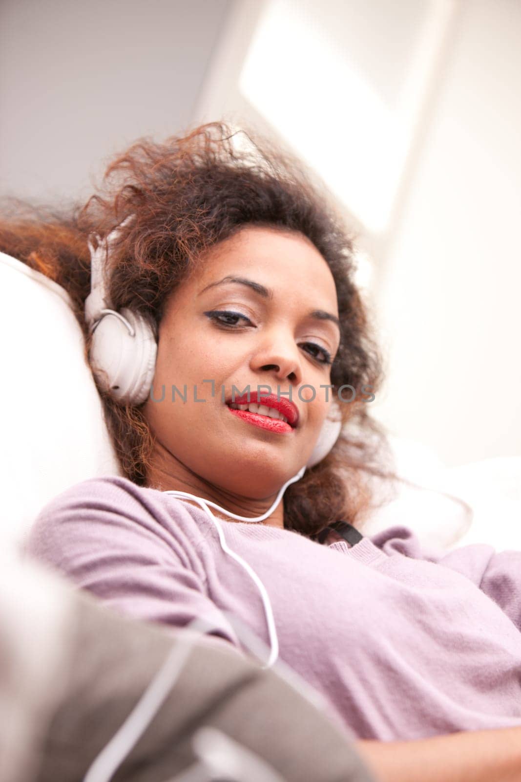 beautiful afroamerican woman on a sofa listenint to the music with her headphones