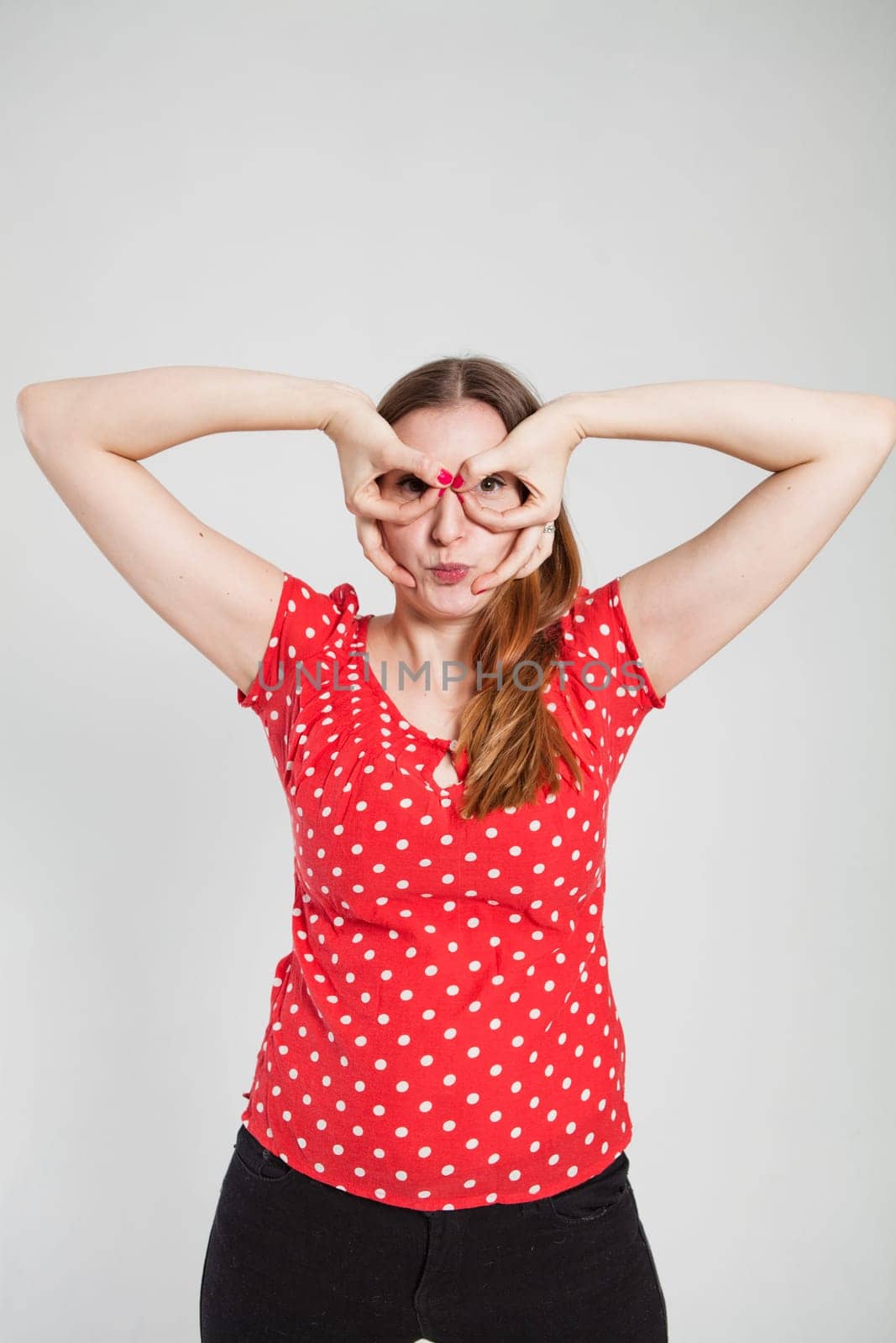 Studio portrait of attractive woman with pursed lips looking through finger goggles