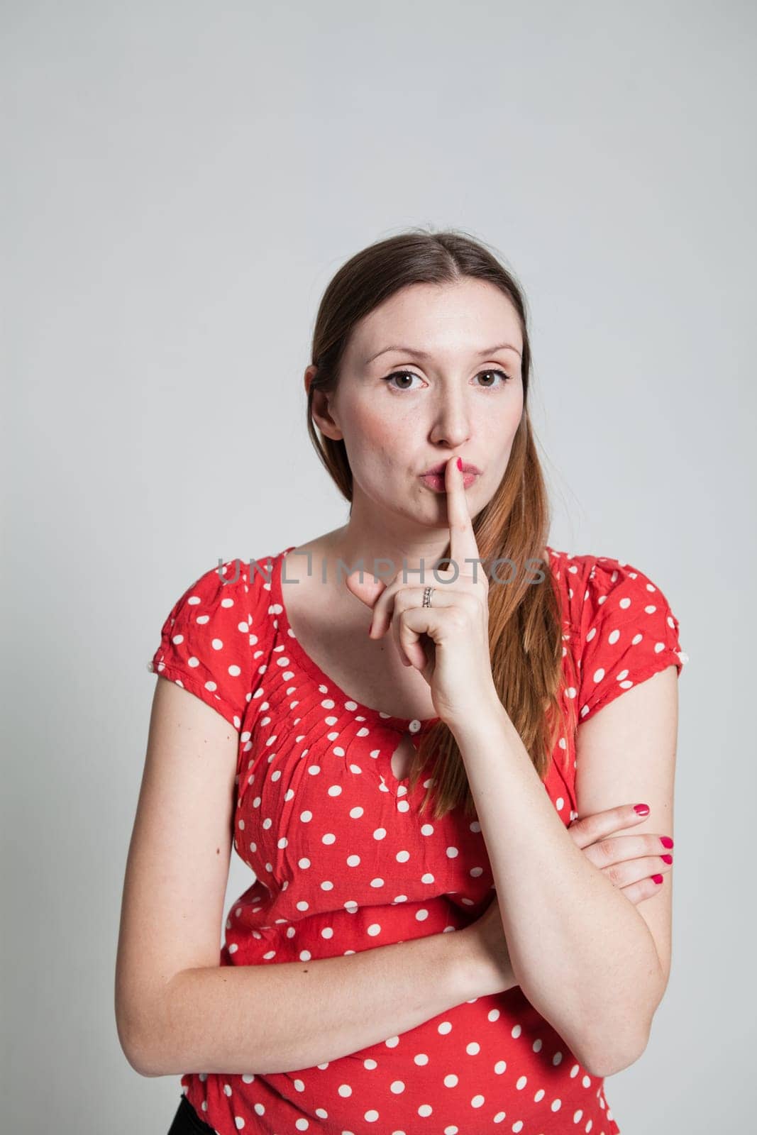 Studio portrait of attractive woman with finger over pursed lips to signal for quiet
