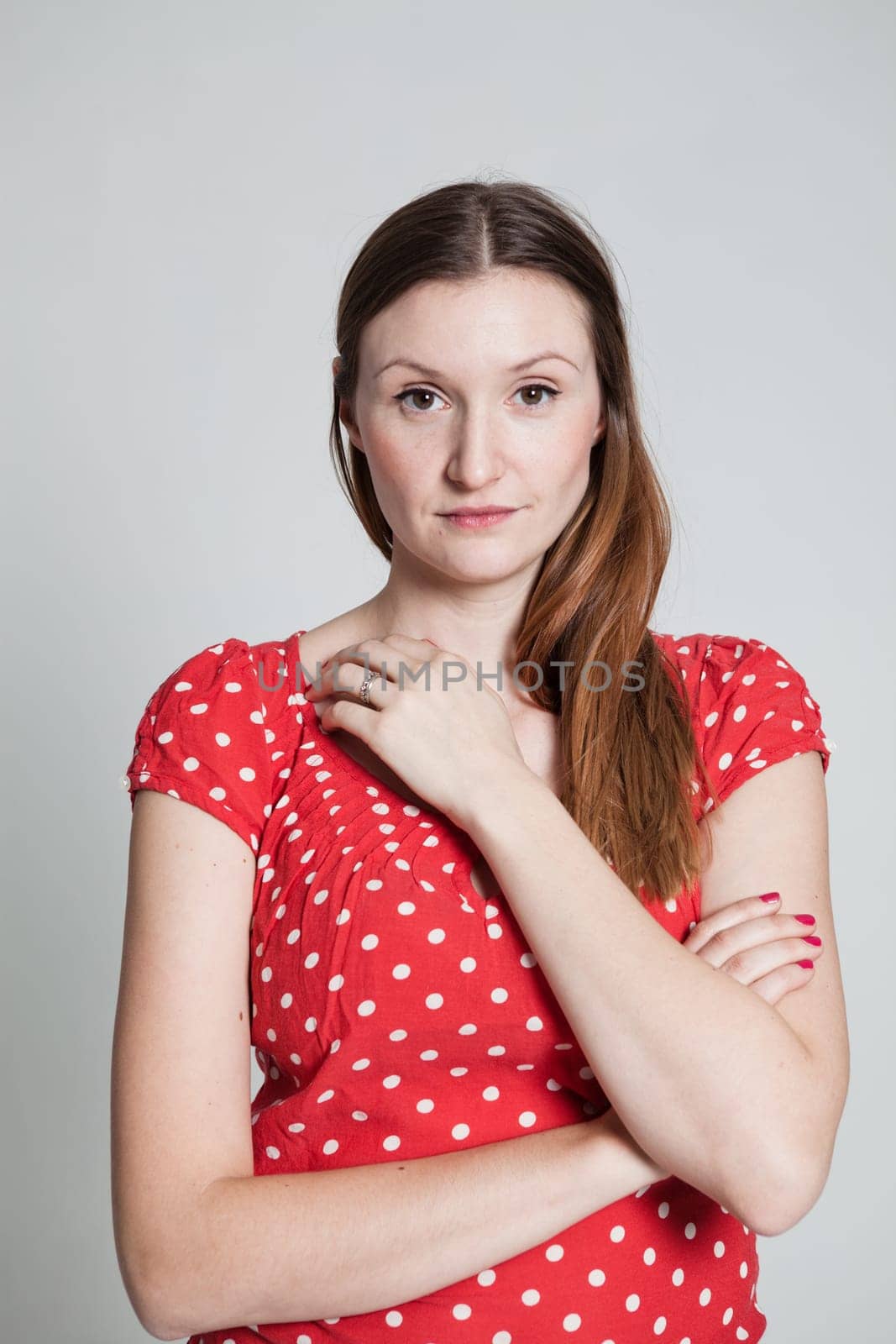 Studio portrait of relaxed and thoughtful looking attractive woman wearing spotty red blouse with arms folded