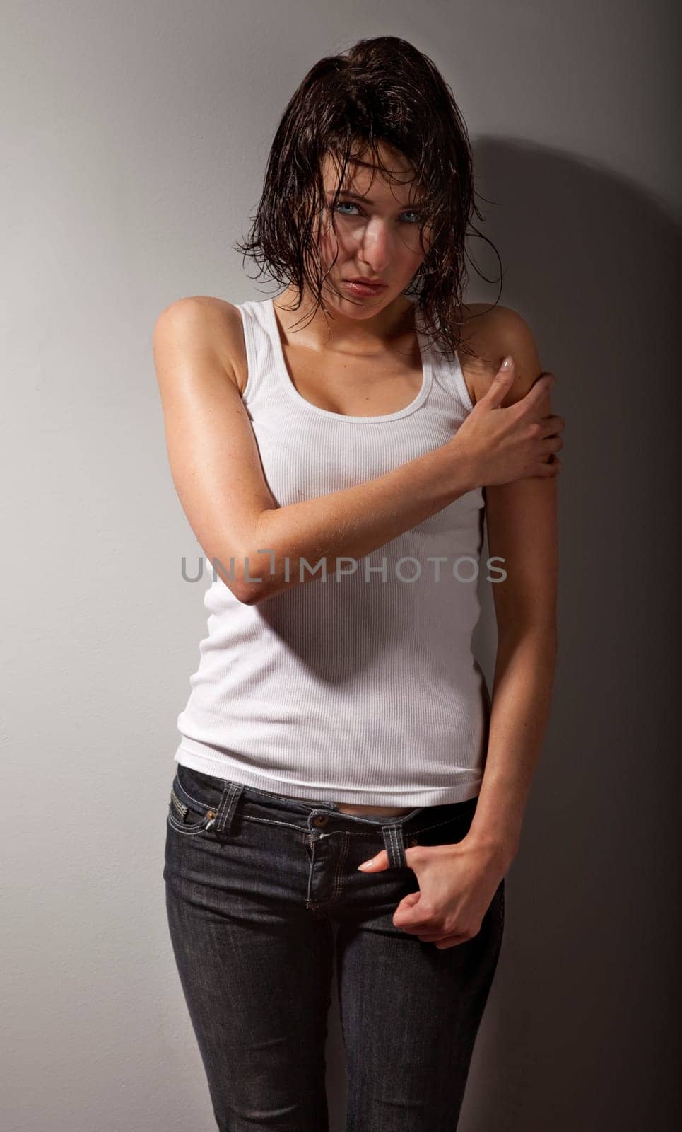 Studio photo of pretty, young, distraught woman stand against wall.