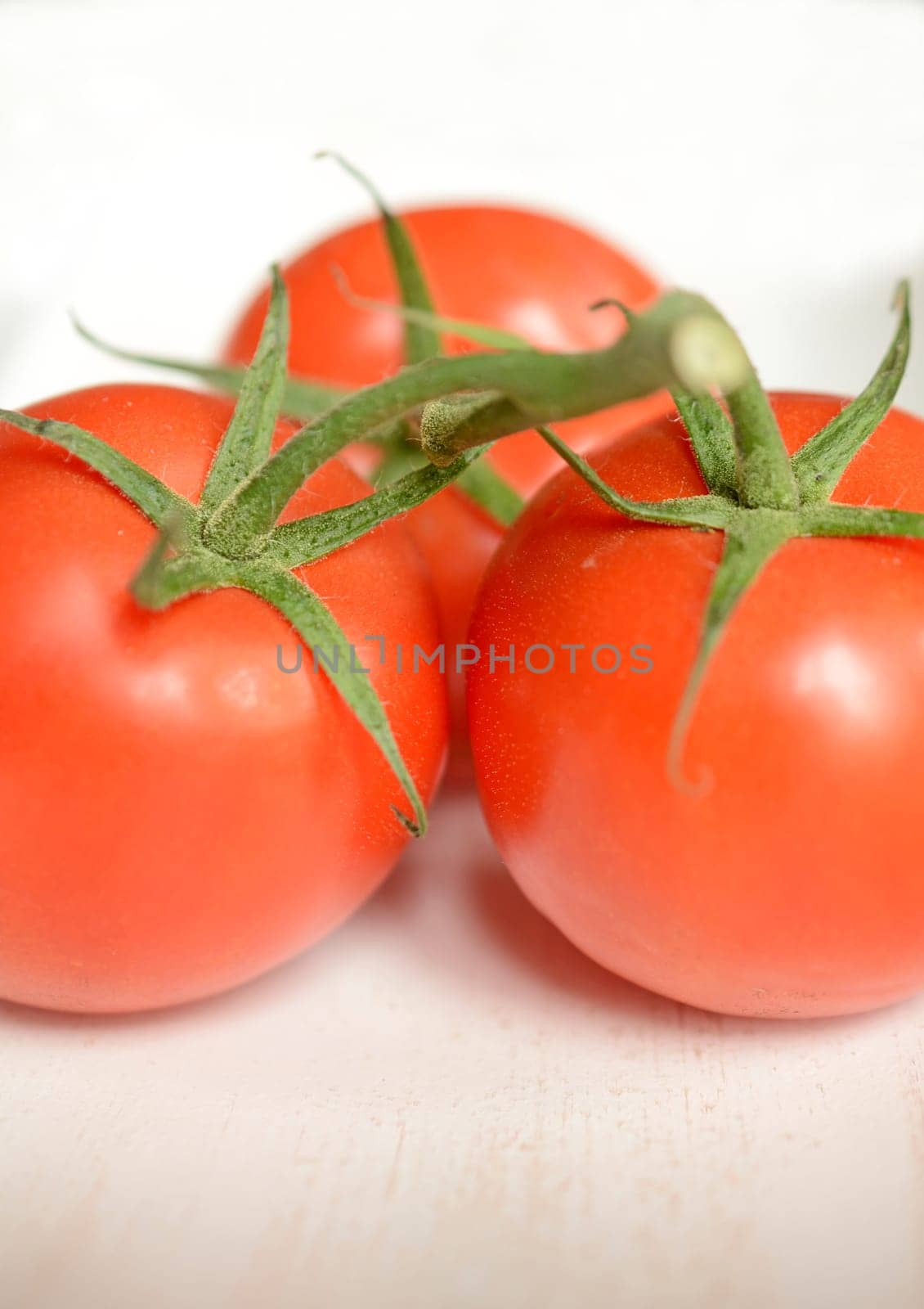 Three tomatoes on a white wooden bowl, close up with selective focus on foreground