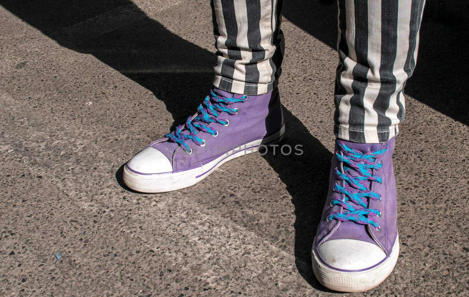 Girl legs with striped pants and purple sneakers on asphalt street surface