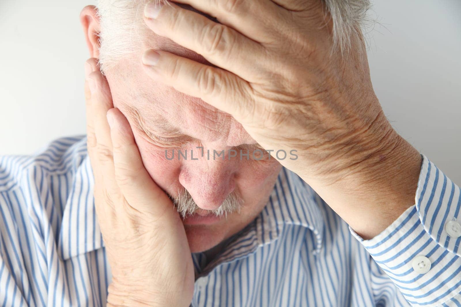older man in pain holds his head with both hands