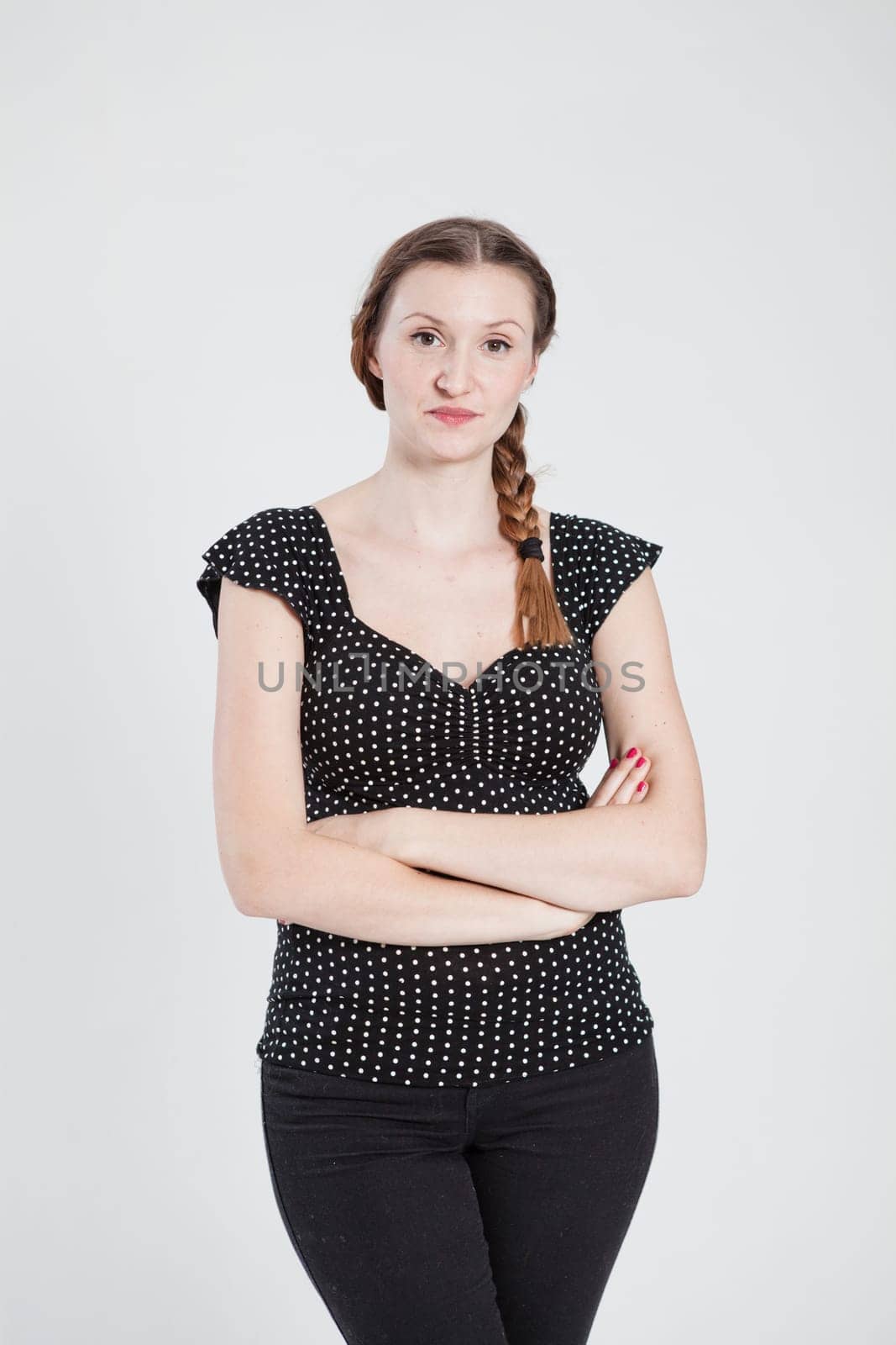 Studio portrait of thoughtful looking attractive woman with pigtail and arms folded