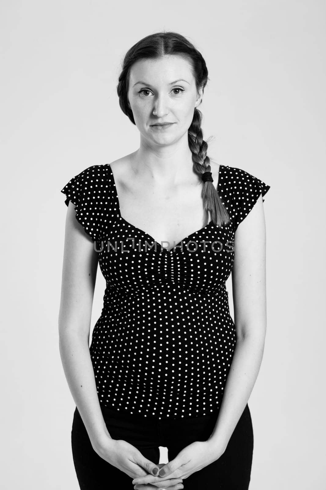 Black and white studio portrait of attractive woman with pigtail holding hands together