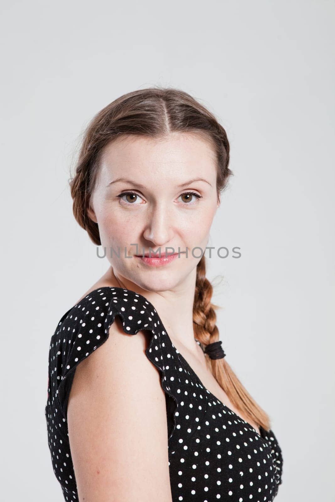 Studio portrait of thoughtful looking attractive woman with pigtail posing for camera in sideways posture