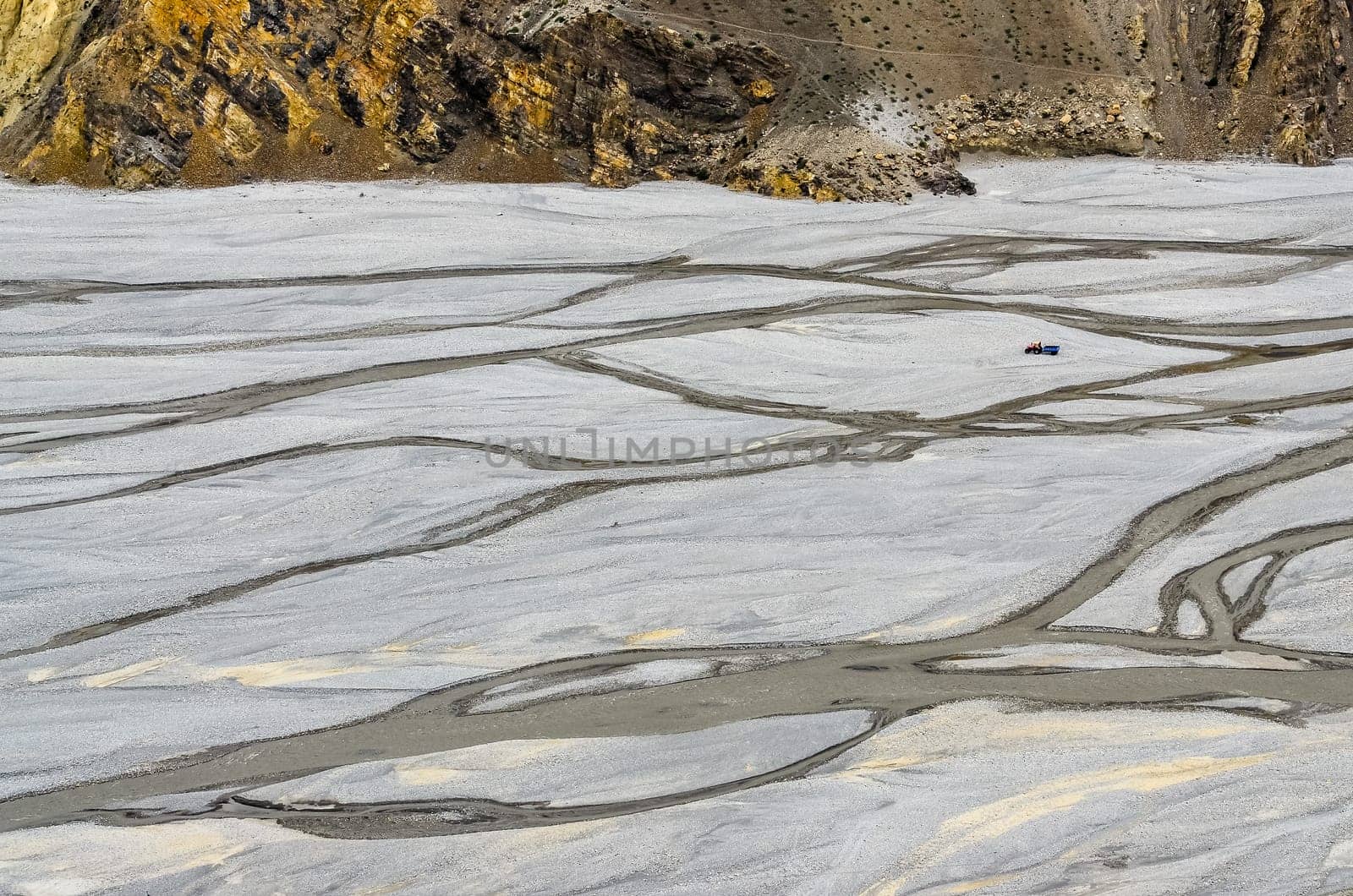 Landscape view of dry eroded river bank with water streams and tractor
