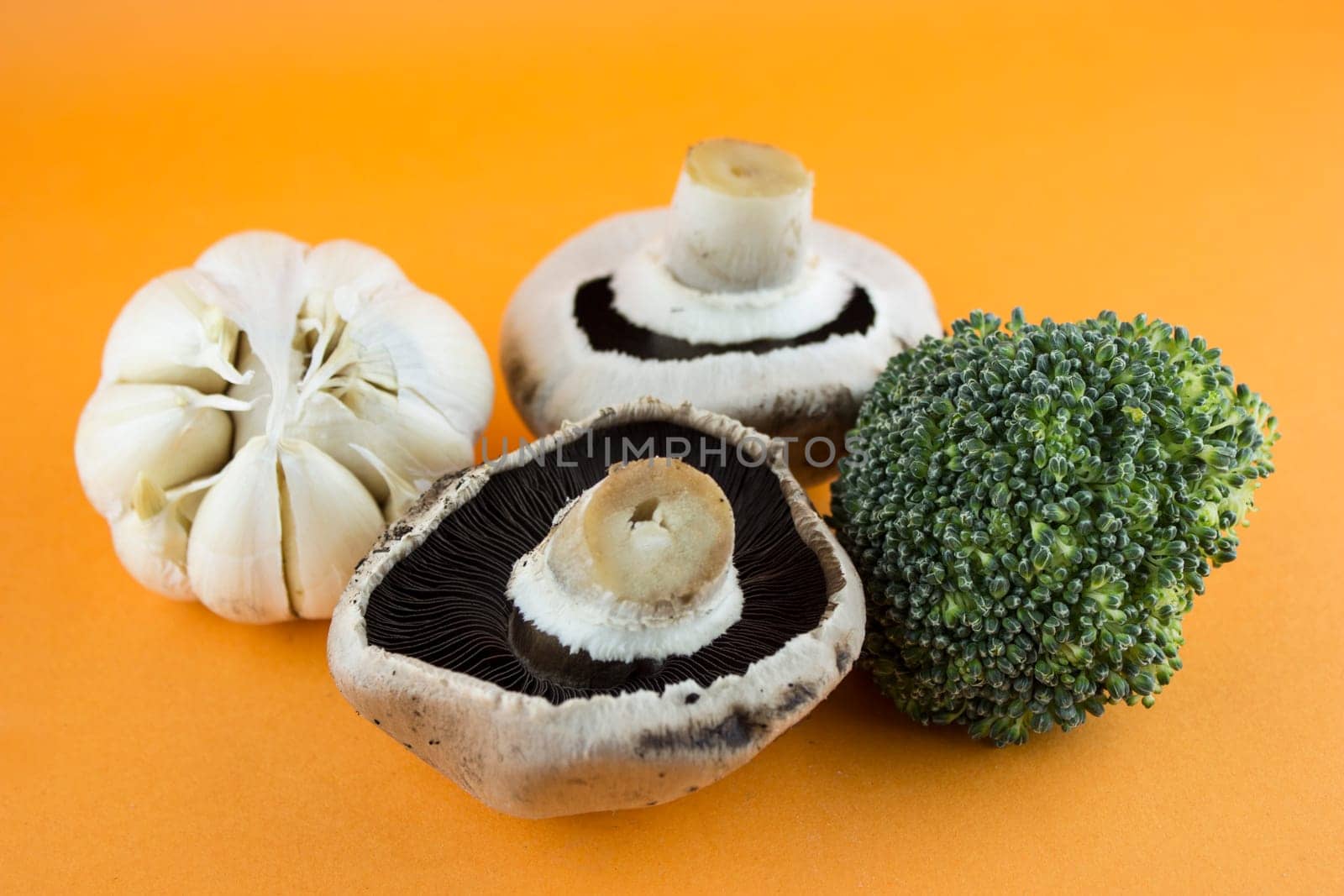 button mushrooms in wooden bowl with garlic, parsley and broccoli on orange background.