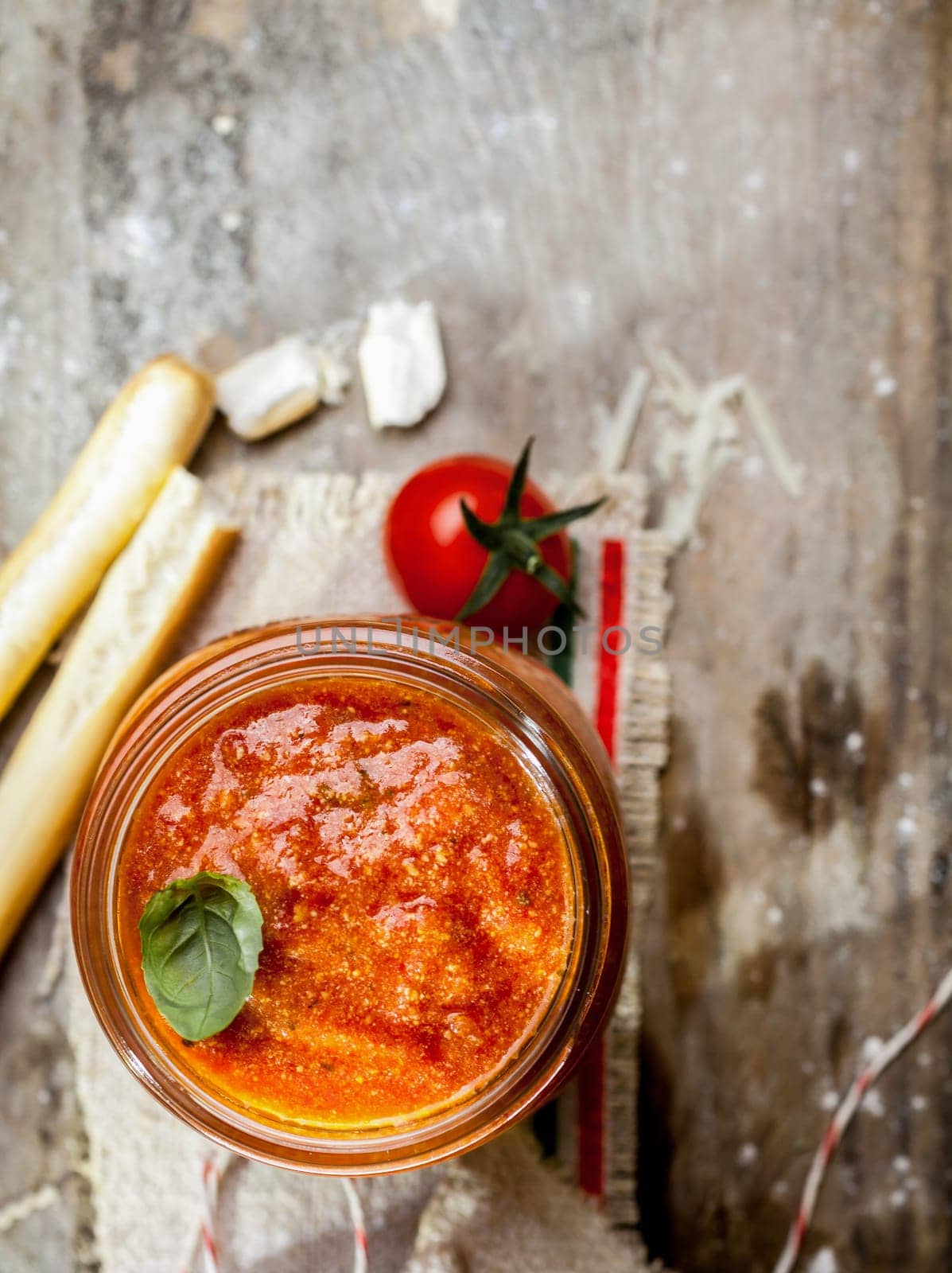 Overhead view of a glass jar of hot spicy tomato relish with grassini or Italian bread sticks on a grungy rustic wooden background with copyspace