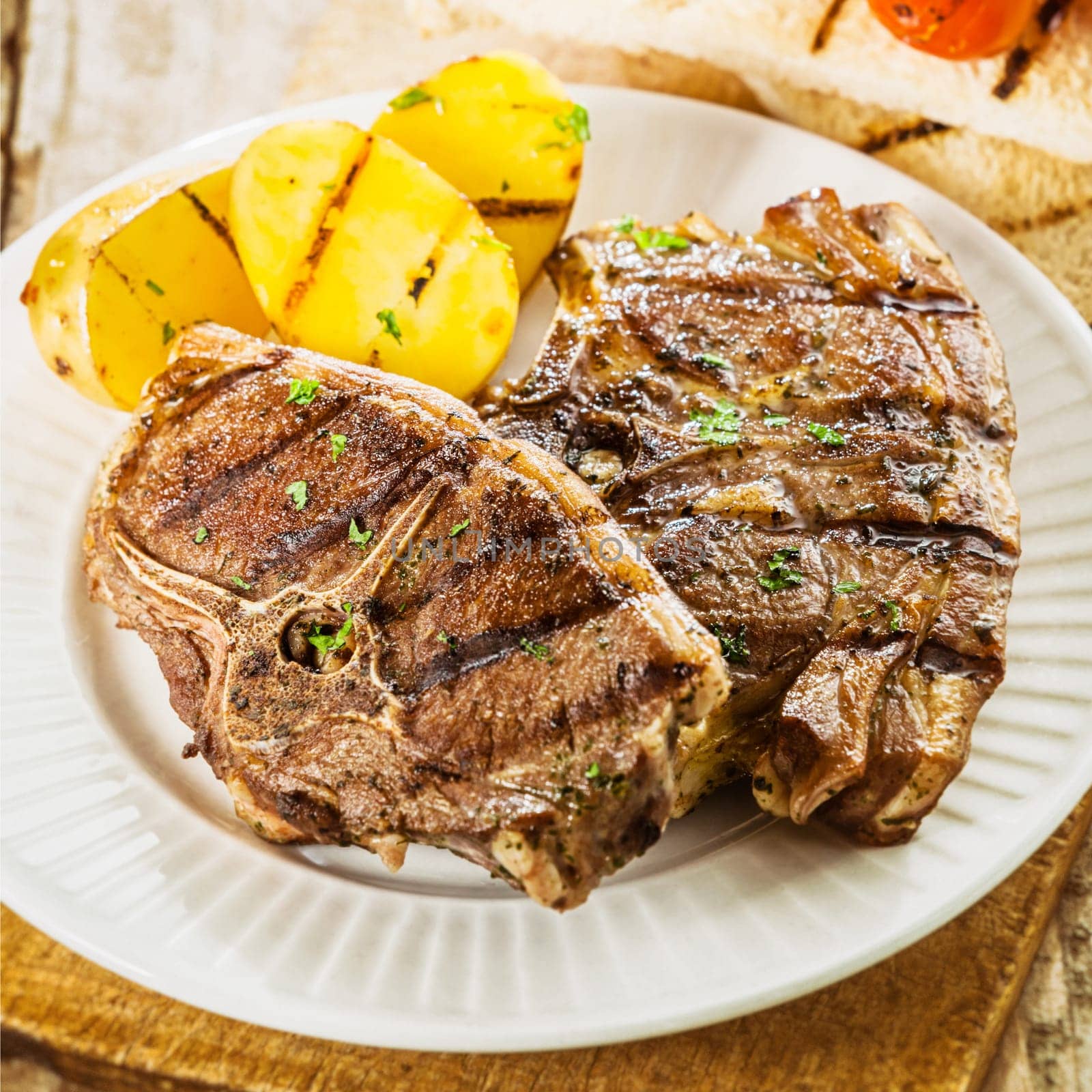 Close up of a serving of two succulent grilled barbecued lamb chops seasoned with fresh herbs served with potatoes at a summer picnic