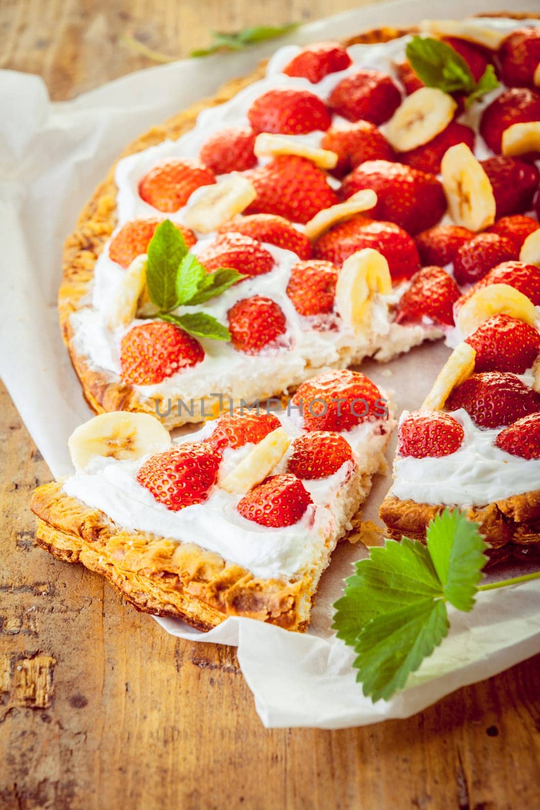 Delicious freshly baked strawberry tart with whipped cream and sliced banana garnish on a crisp golden pastry pie crust with a single slice removed