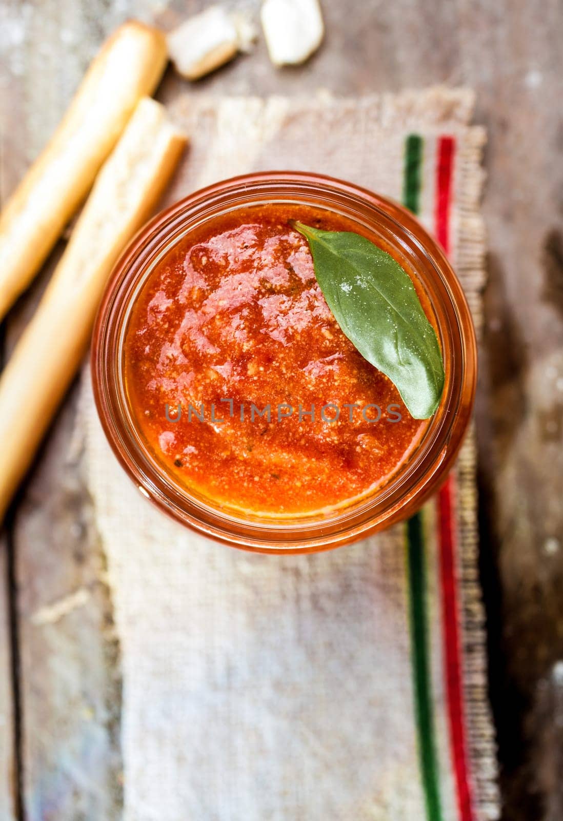 Grissini bread sticks with a glass jar of savory spicy tomato relish for a tasty Italian appetizer, overhead view with copyspace
