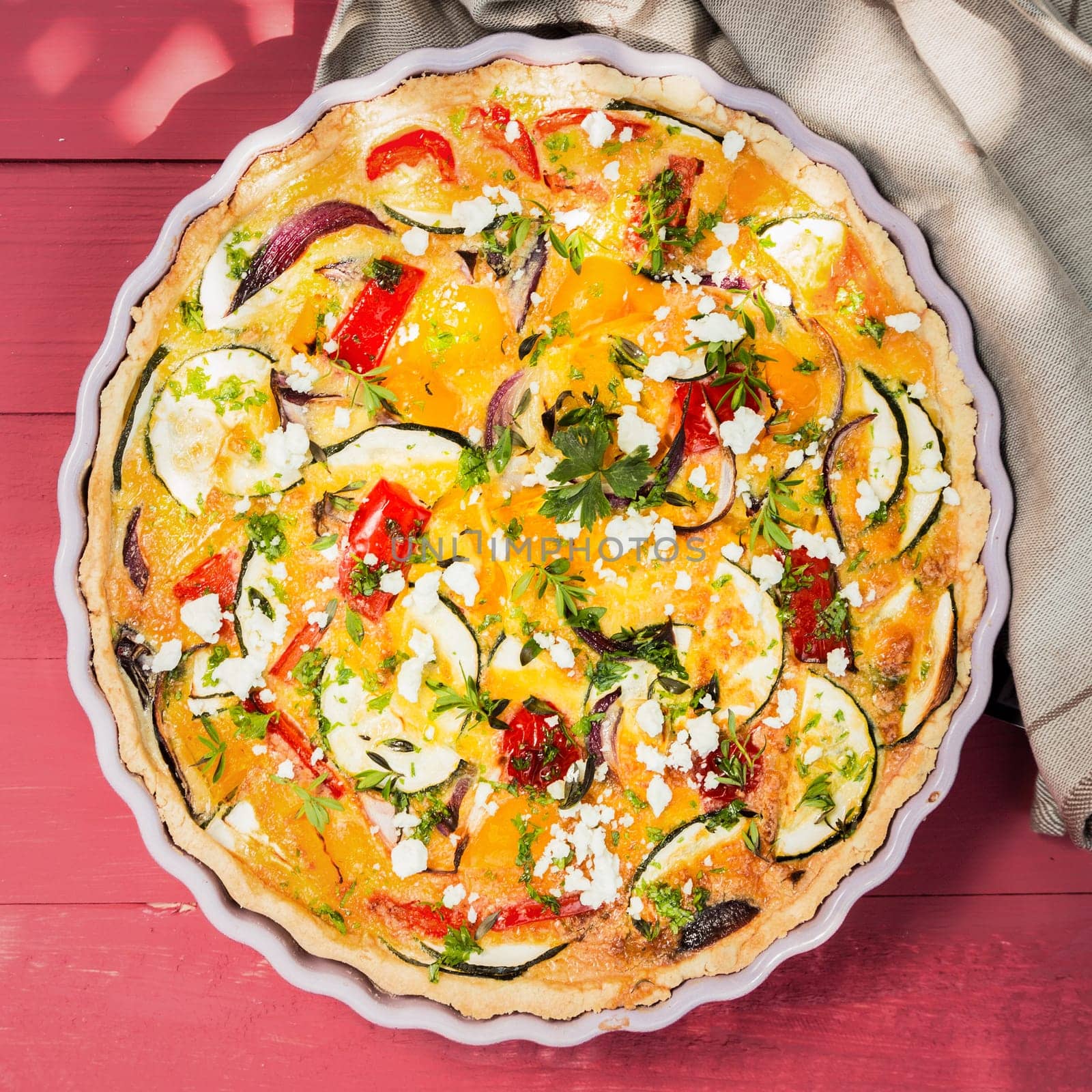 Delicious savory tart or quiche with brinjals or eggplant, pepper, tomato and cheese sprinkled with fresh chopped herbs, overhead view