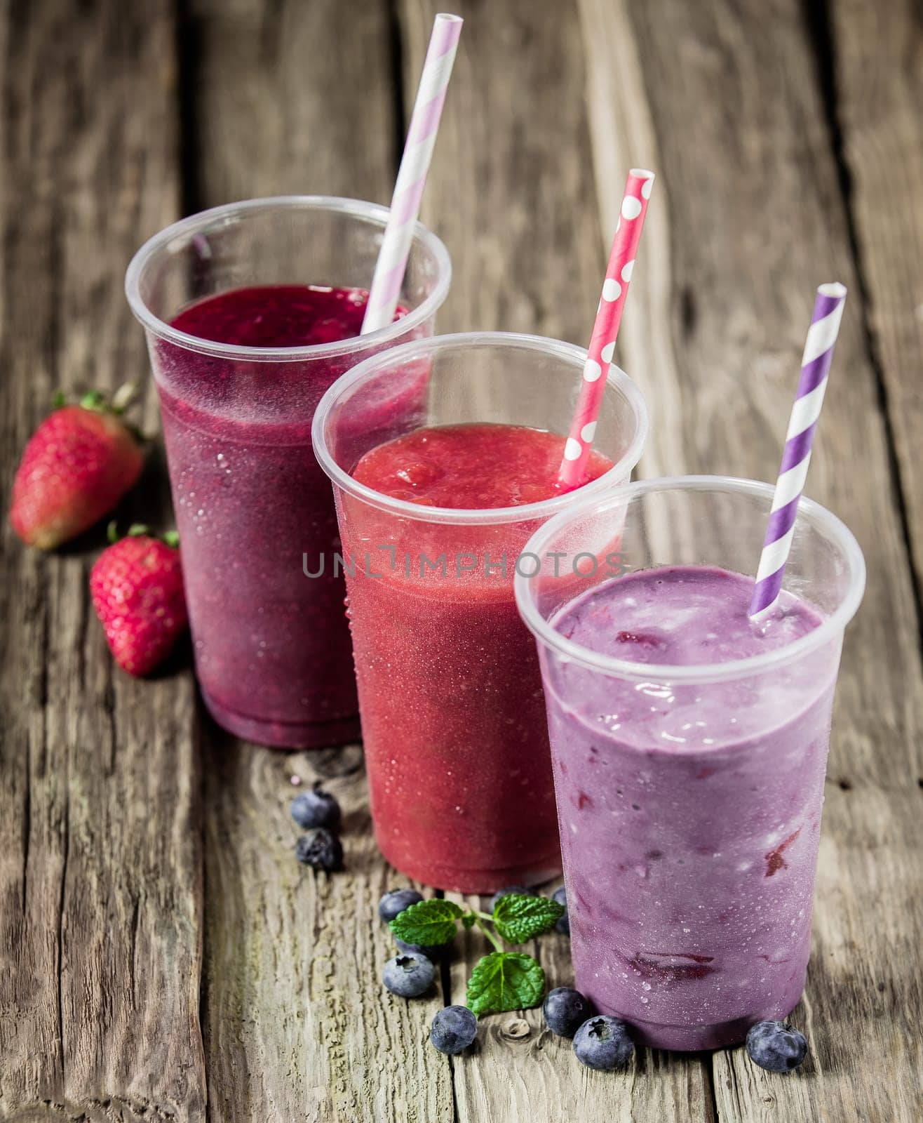 Trio of delicious berry smoothies with fresh strawberries and blueberries in a rustic country kitchen, high angle view