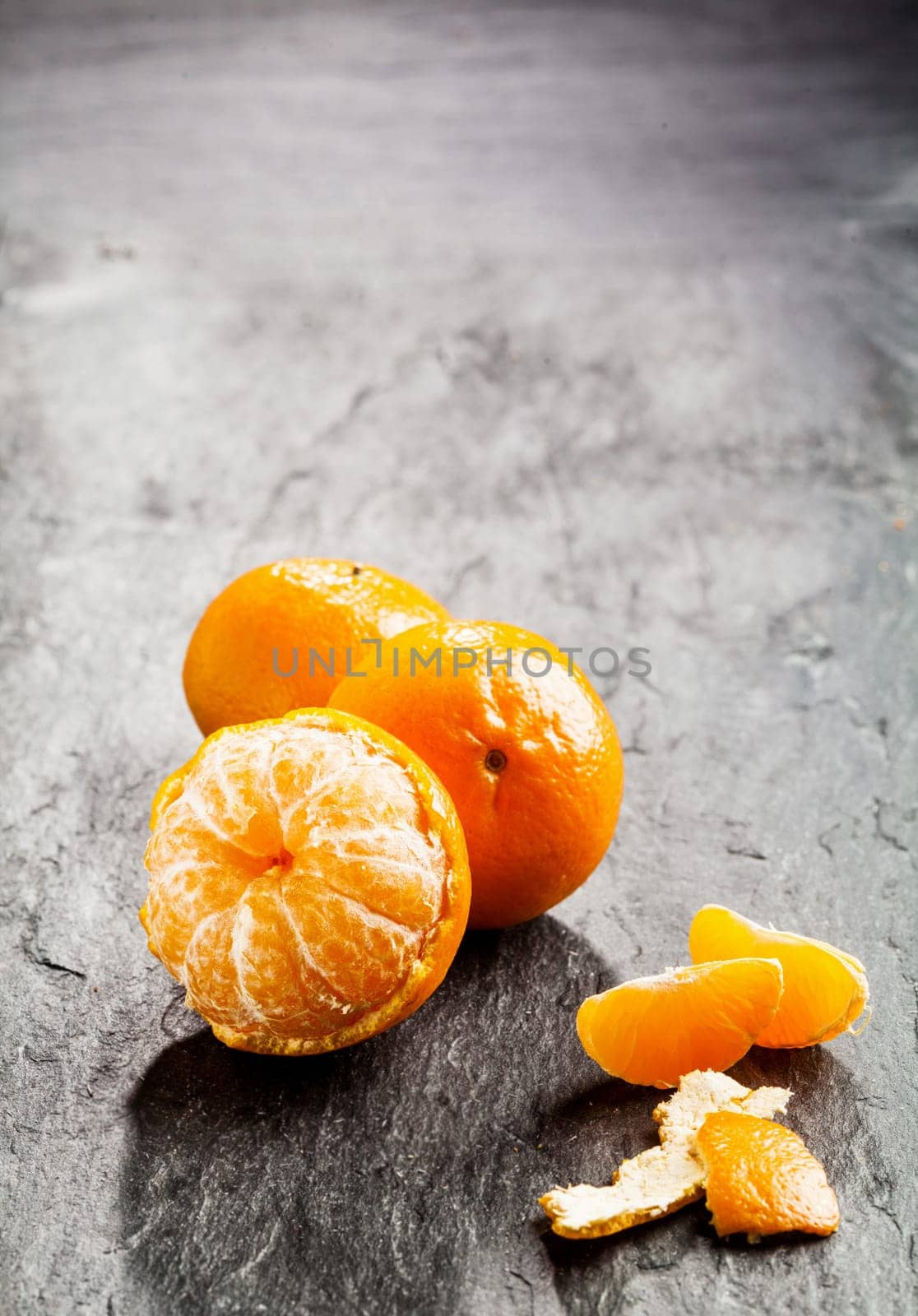 Peeled fresh sweet nectarine, tangerine or clementine with scattered loose peel and segments on a dark background with copyspace