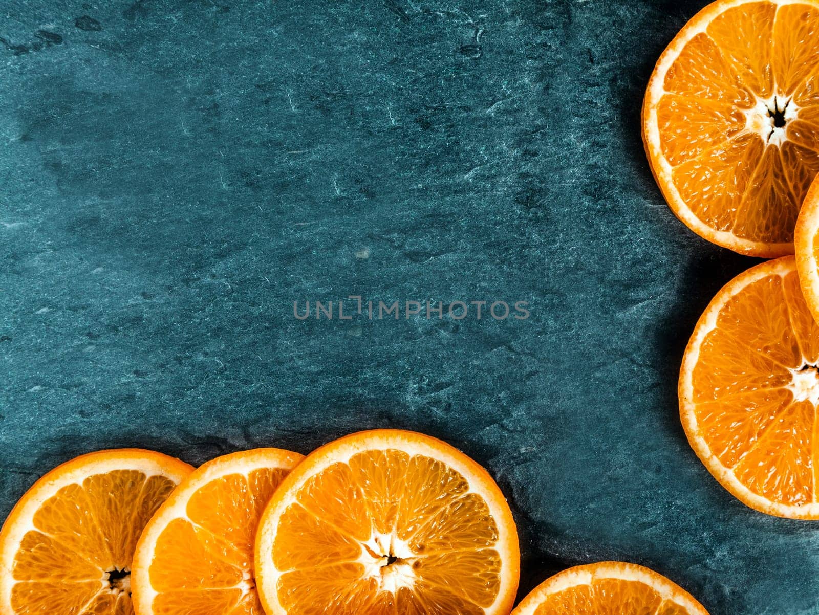 Border of fresh juicy orange slices arranged on two sides on a dark textured slate background with copyspace for your text