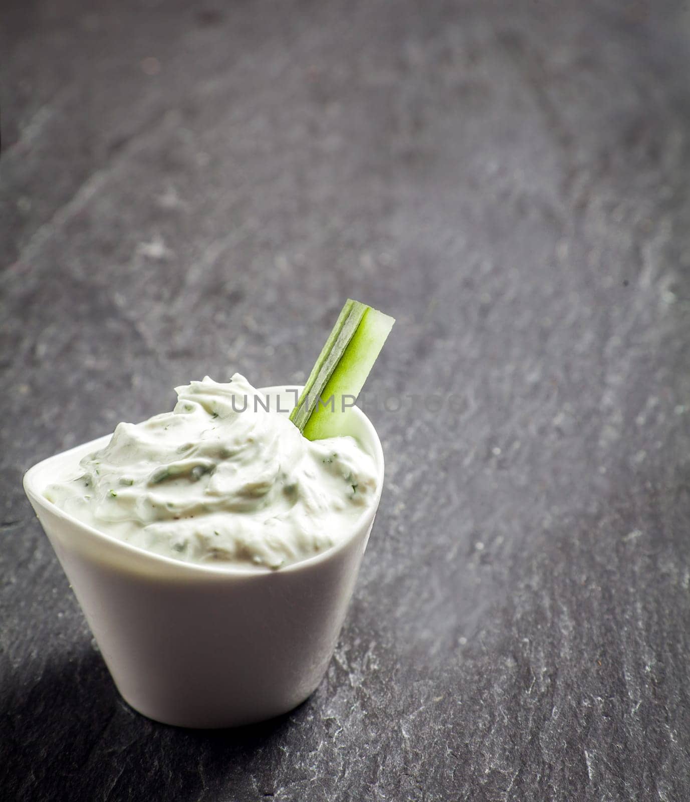 Delicious creamy vinaigrette and cottage cheese sauce in a ceramic dish with a cucumber crudites or baton for a healthy snack or appetizer on grey slate with copyspace