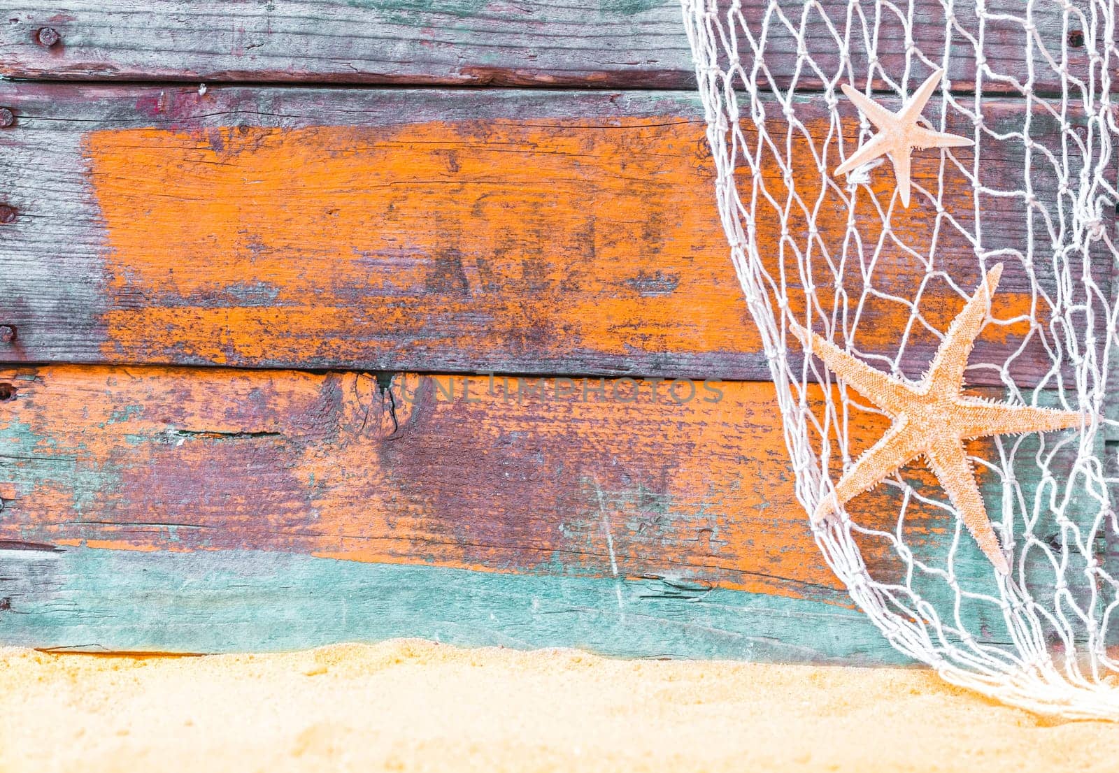 Nautical starfish background with rustic grunge weathered blue painted wooden boards, fishing net and golden beach sand, copyspace for text