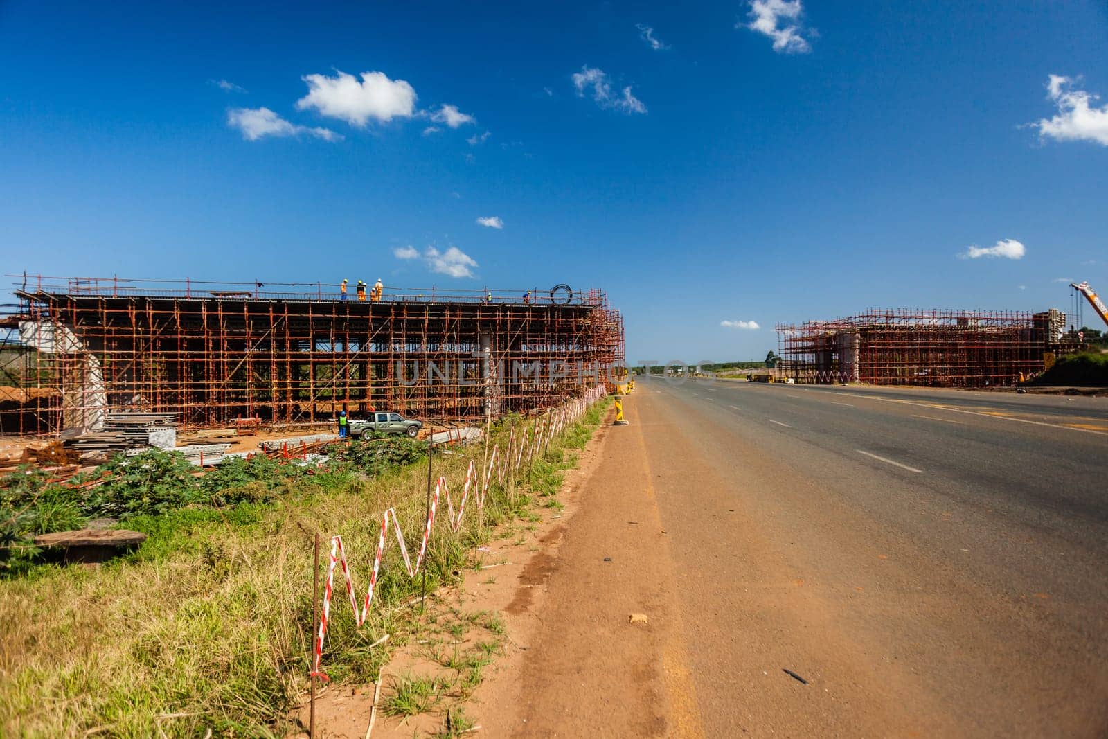 New bridge construction over road highway with building materials and machines on roadside site.