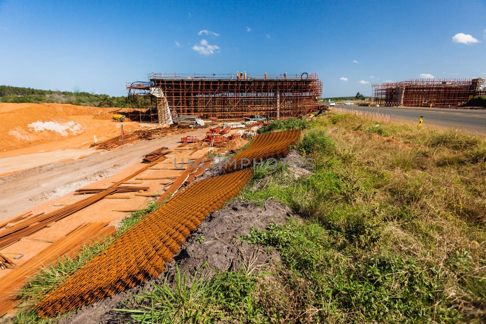 New bridge construction over road highway with building materials and machines on roadside site.