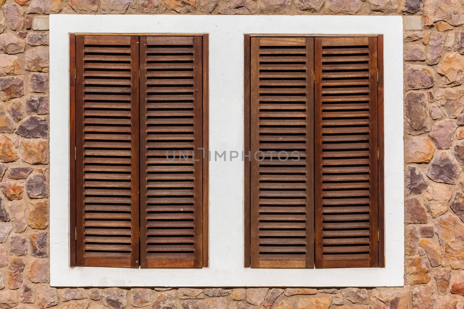 Windows in stone wall of home with wood shutters for weather,privacy and security
