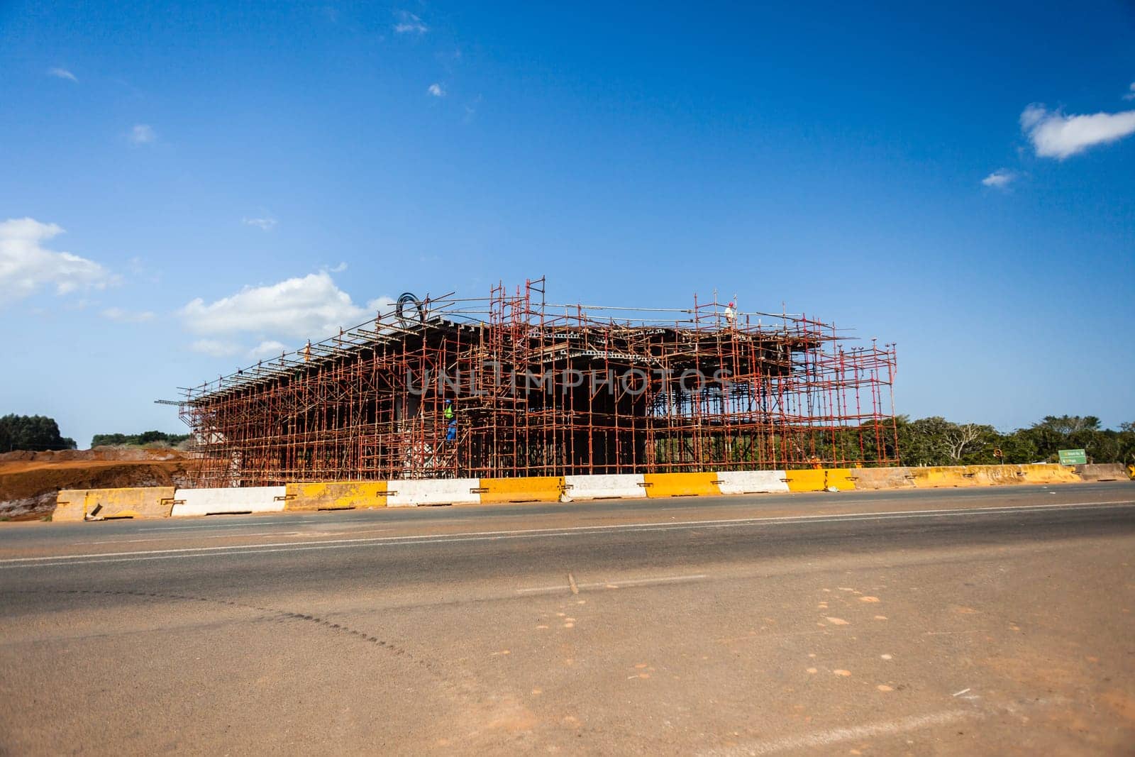 New bridge construction over road highway with building materials and machines on roadside site.