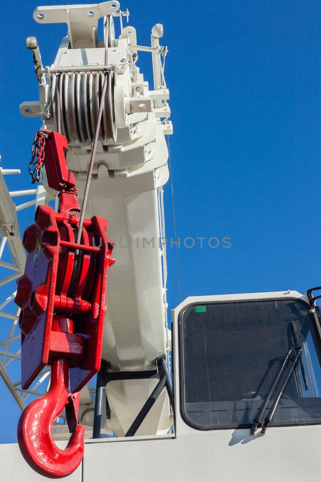 Mobile crane vehicles red hoist hook and white painted extension arms and operator cabin on vehicle against blue sky
