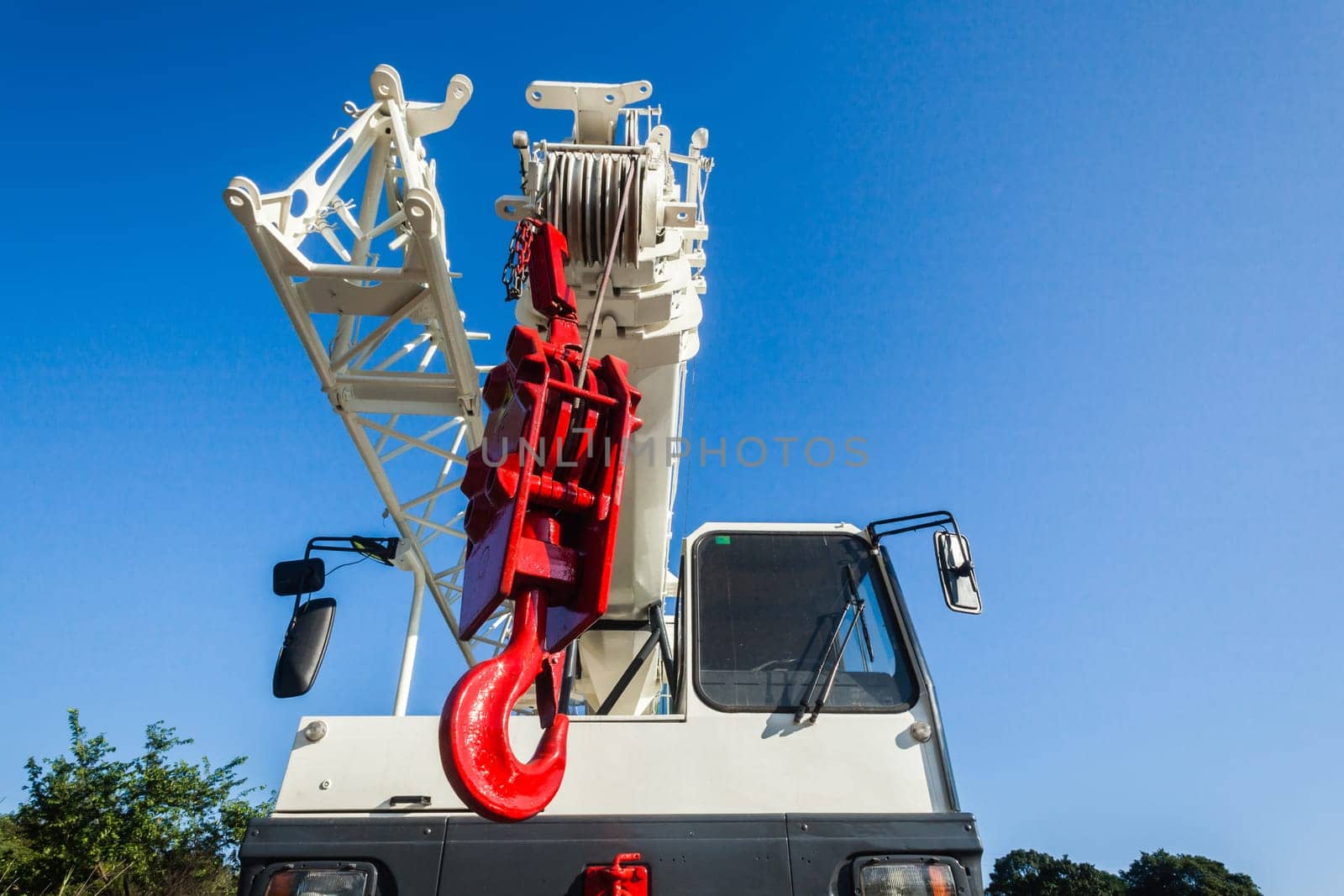 Mobile crane vehicles red hoist hook and white painted extension arms and operator cabin on vehicle against blue sky