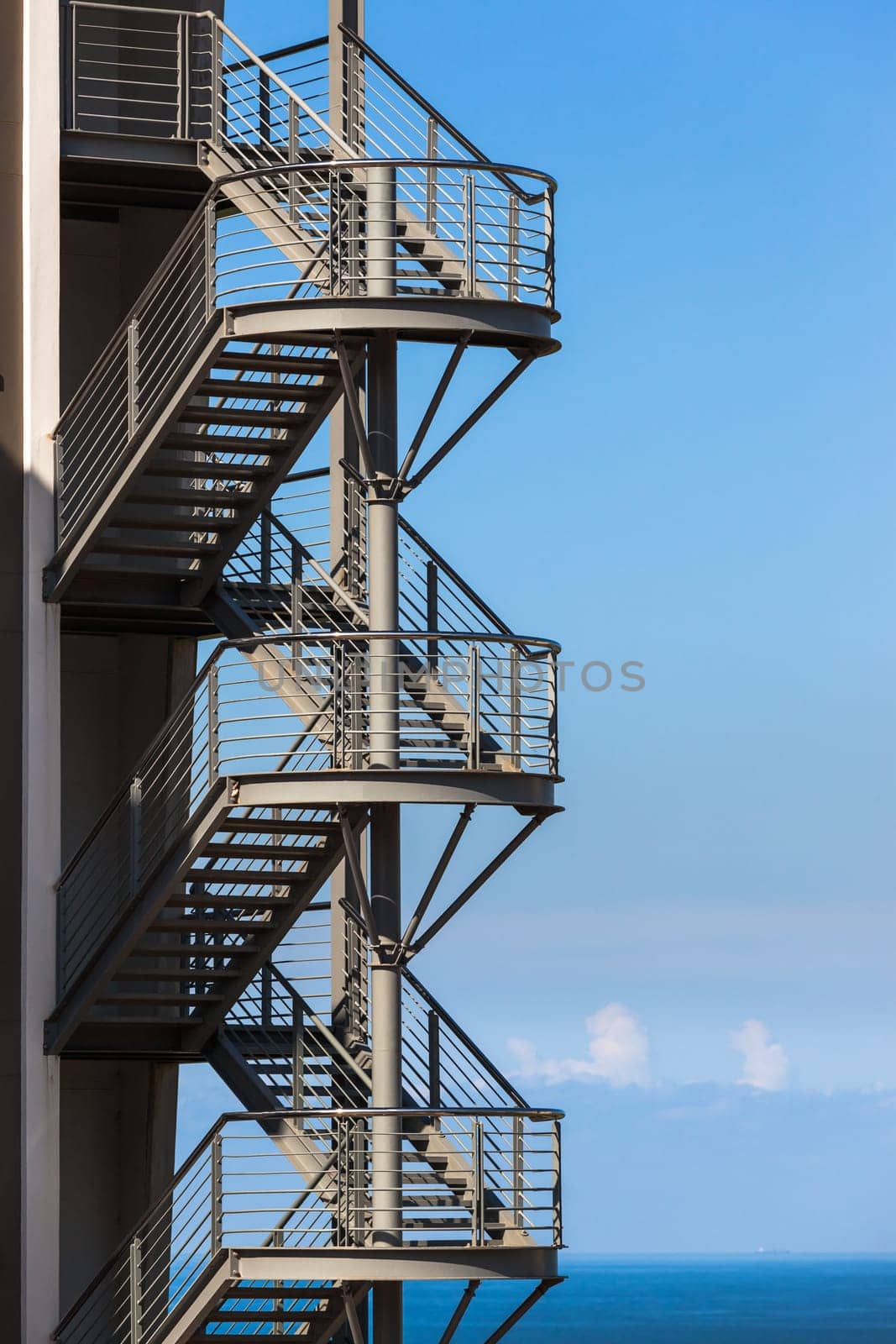 Building section back metal stairway fire-escape exit overlooking blue ocean.