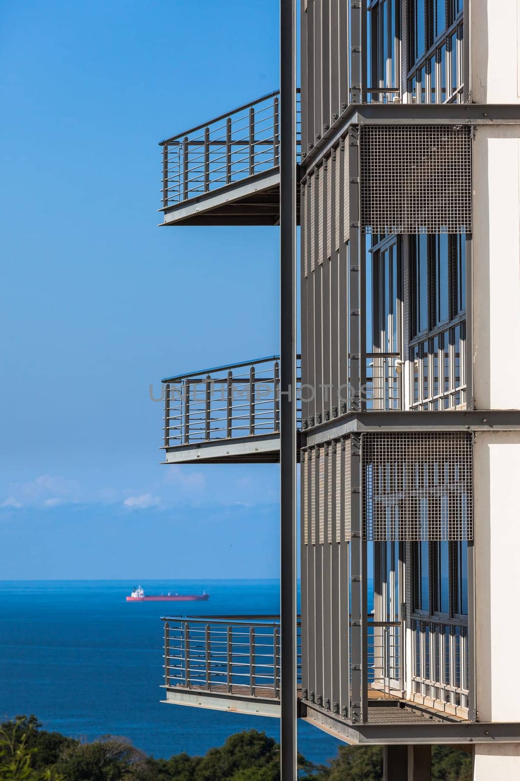 Building section of three porch verandahs overlooking blue ocean with distant ship