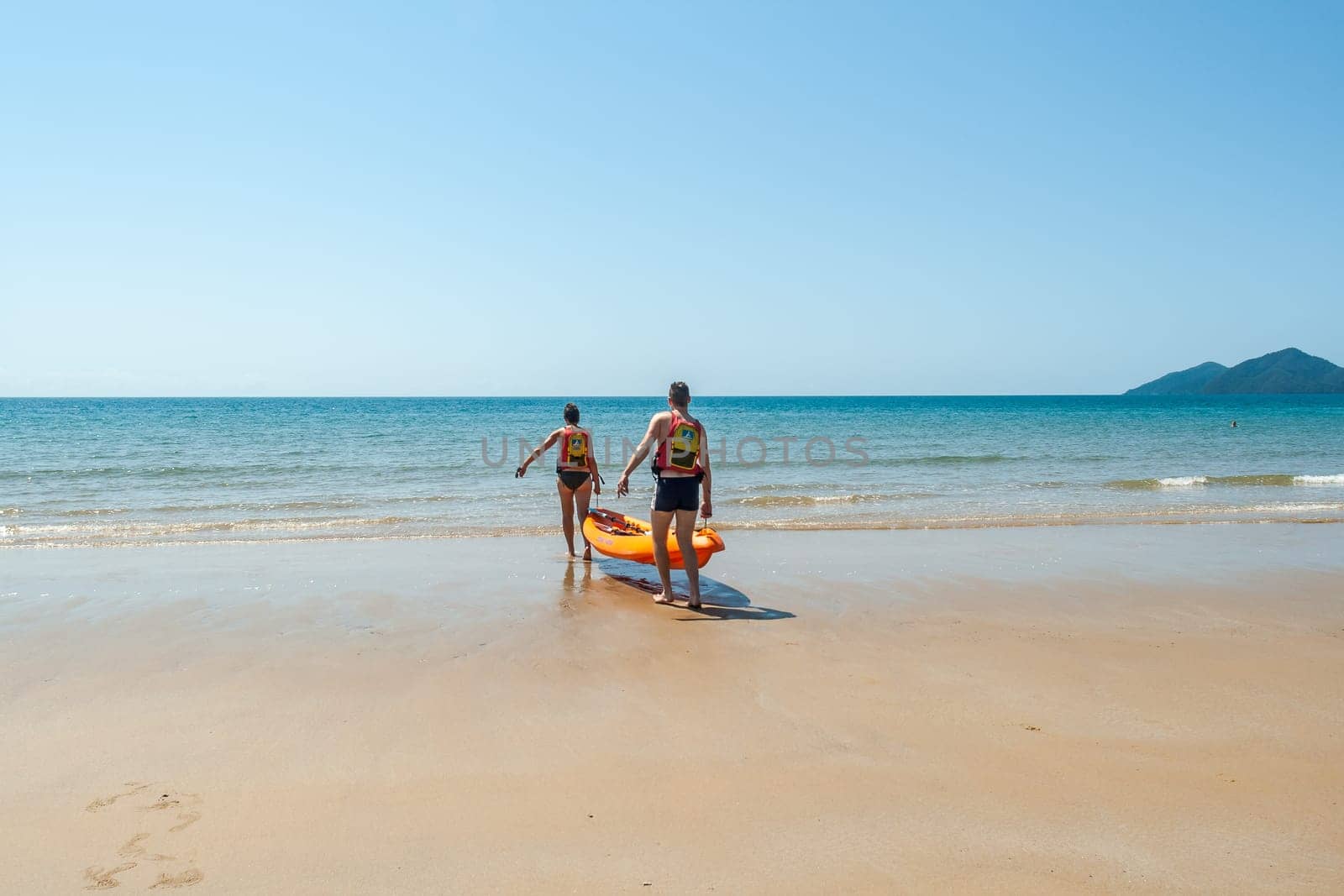 Couple man woman unidentified carrying kayak into tropical waters at  mission beach nearby Cairns Queensland Australia